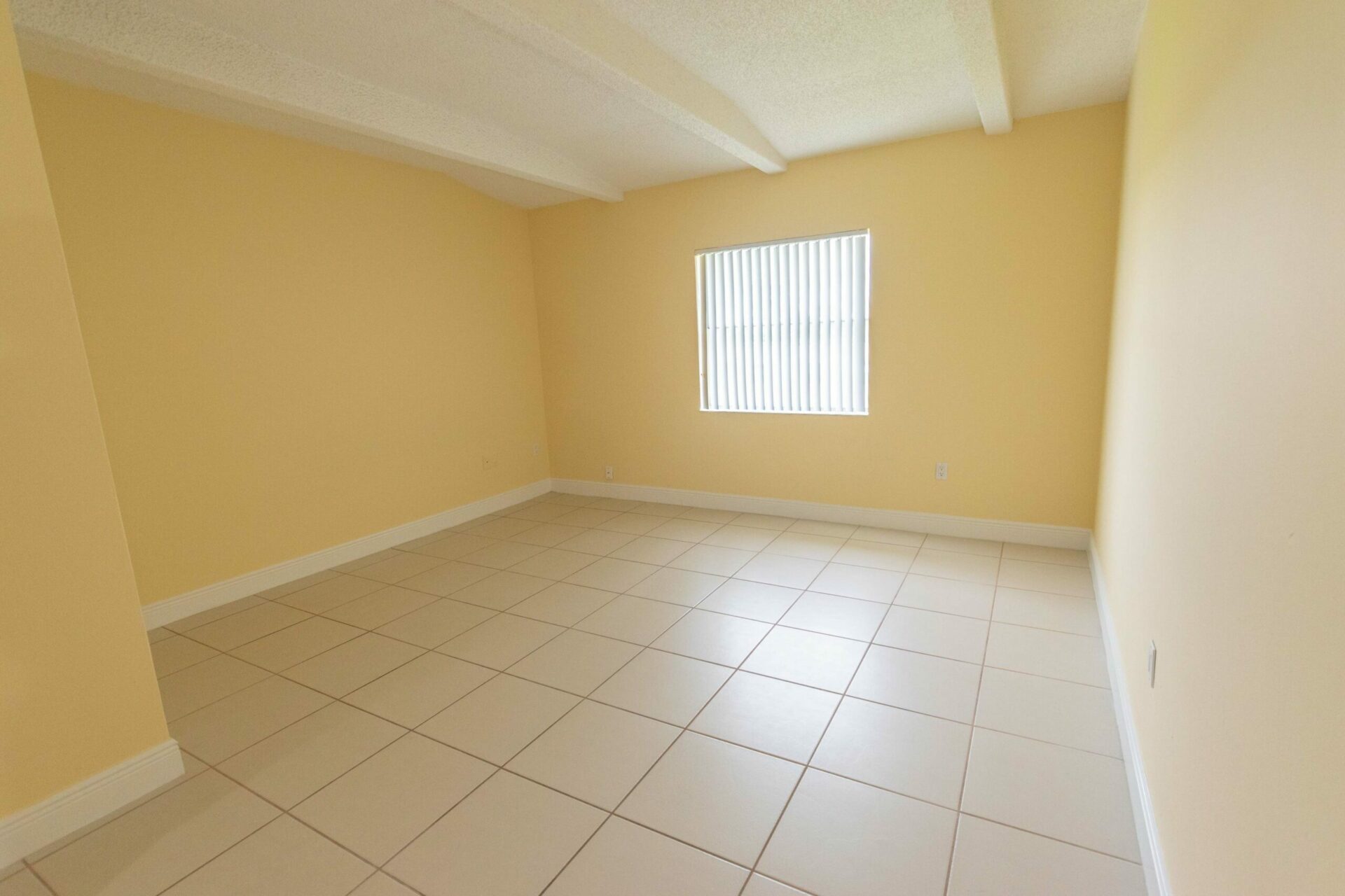 Spacious area with a large window, yellow walls, and white tiles in a Miami, FL apartment.