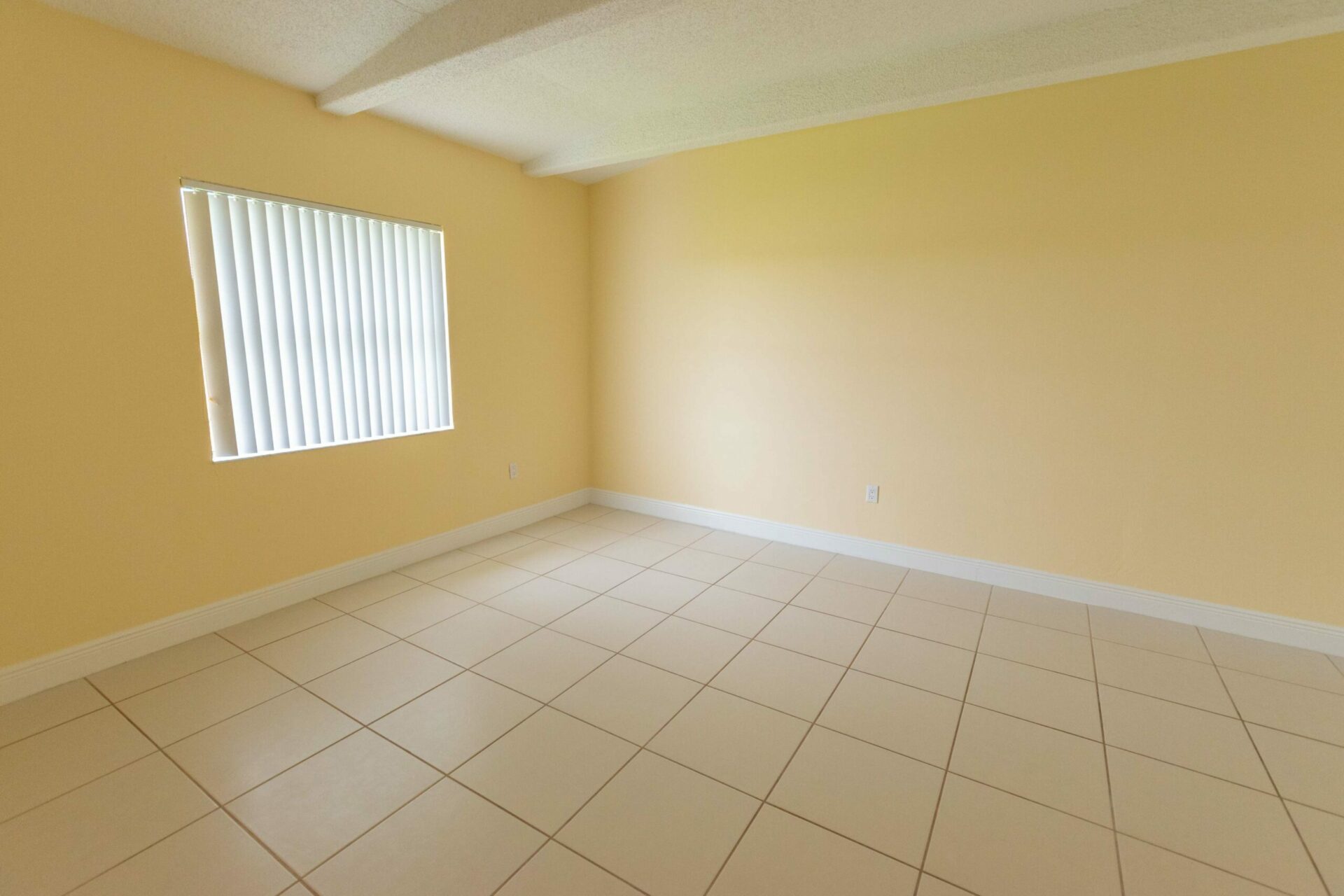 Spacious area with a large window, yellow walls, and white tiles.