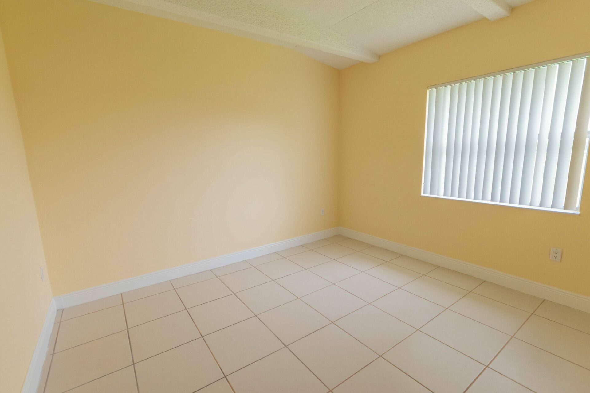 Spacious room with light yellow walls, a window, and white tile flooring.