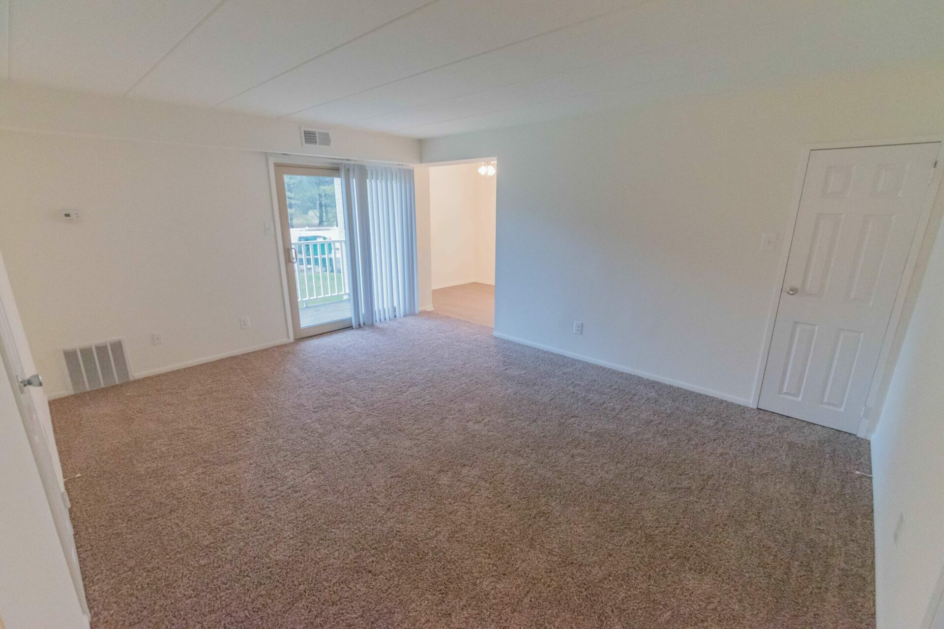 Living room area of an apartment unfurnished, fitted with carpet flooring, a high ceiling, and slide door to patio