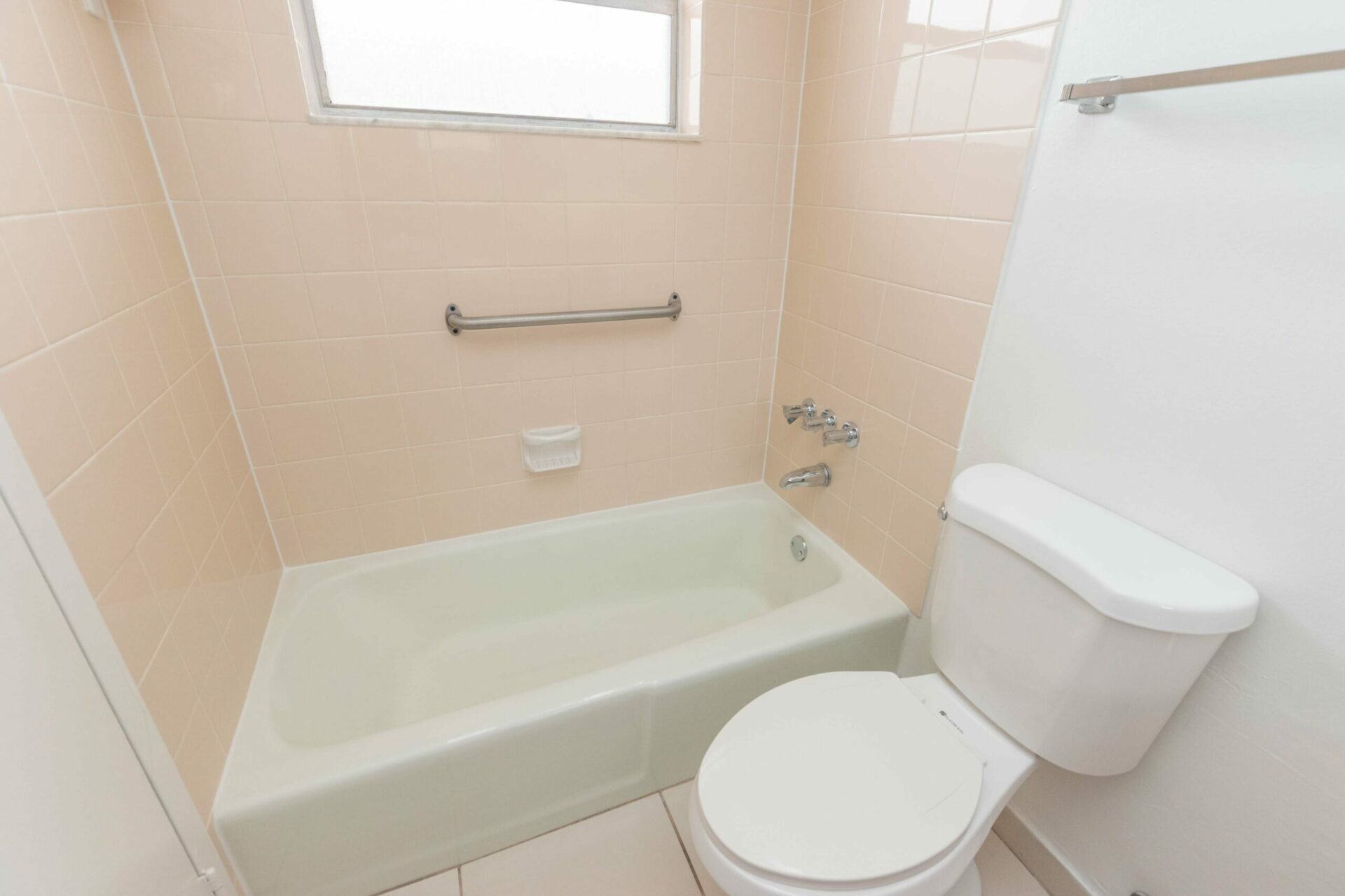 Bathtub with light pink tiles and a toilet in a bathroom of an apartment.