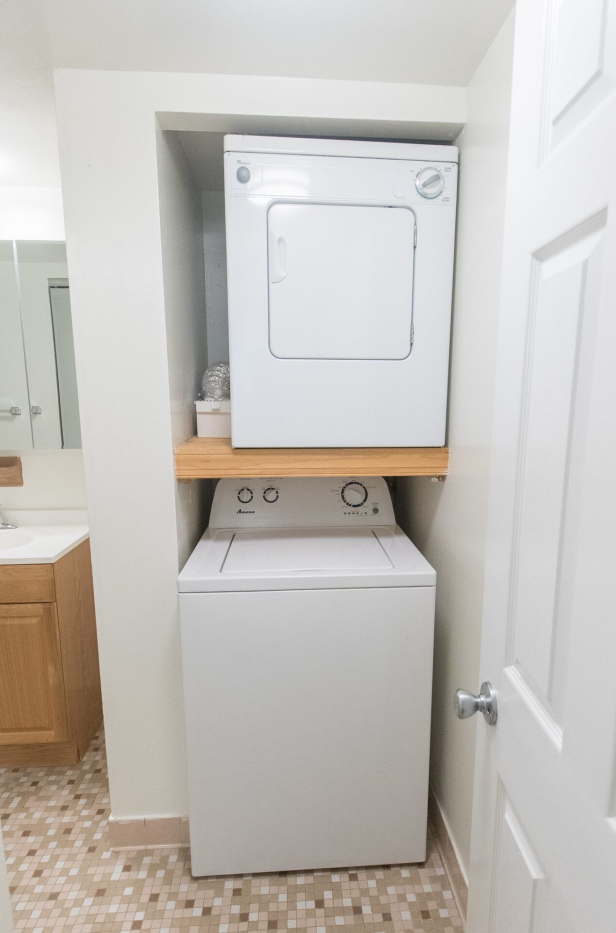In-unit washer/dryer area of an apartment, fitted with a washer, a dryer, and tiled flooring