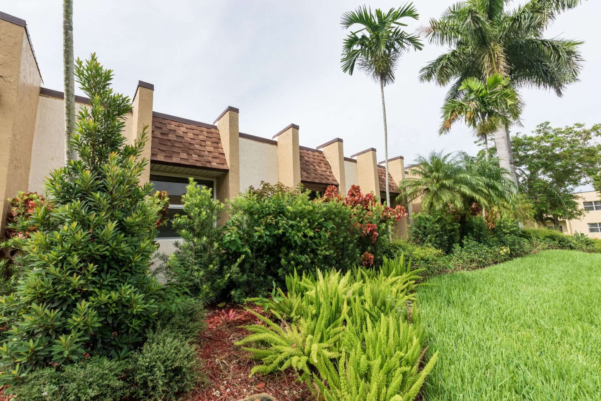 Exterior of a Green Briar West apartment with various types of plants and palm trees.