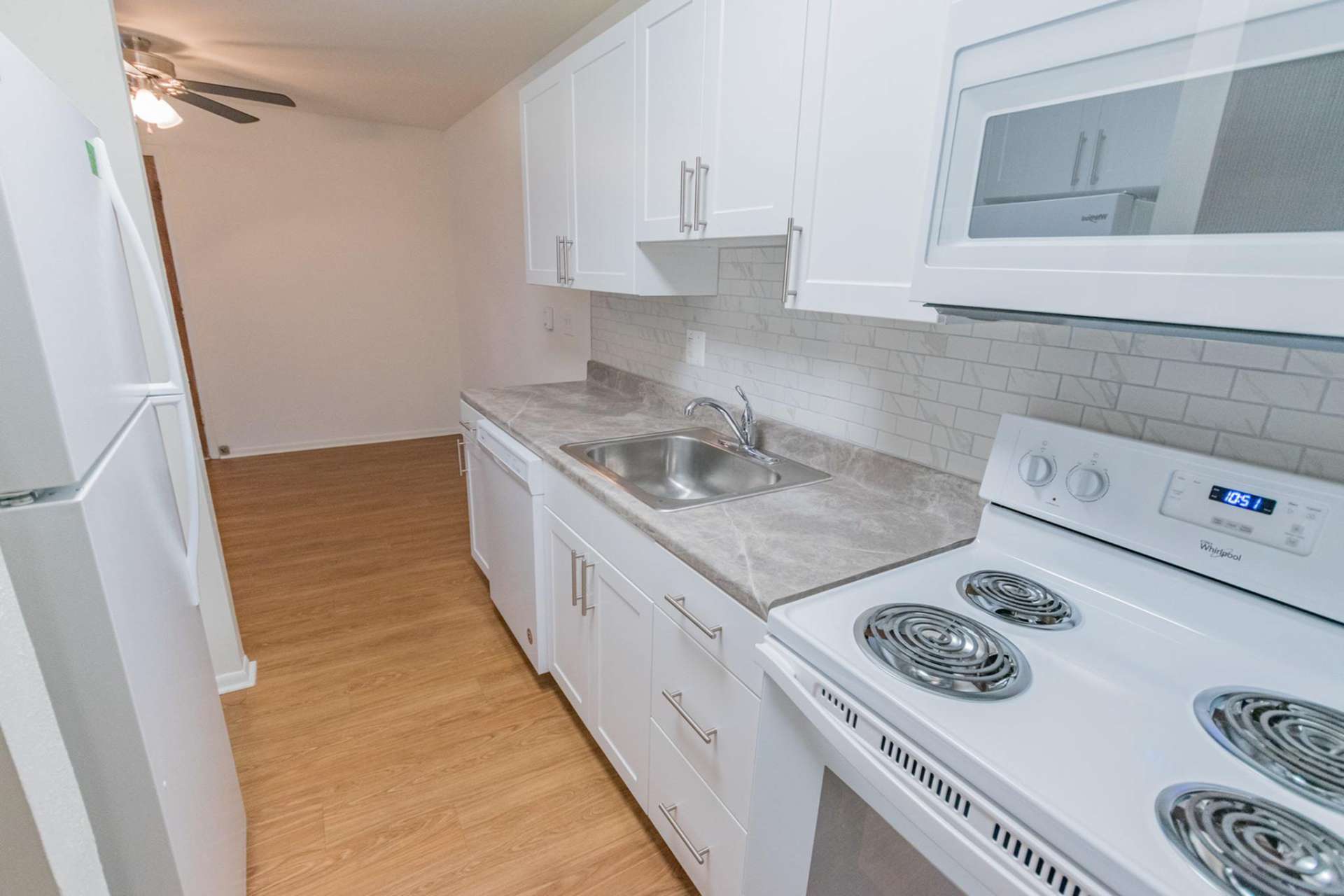 Kitchen area with wooden floors, a microwave, stovetop oven, and fridge with hardwood floors.
