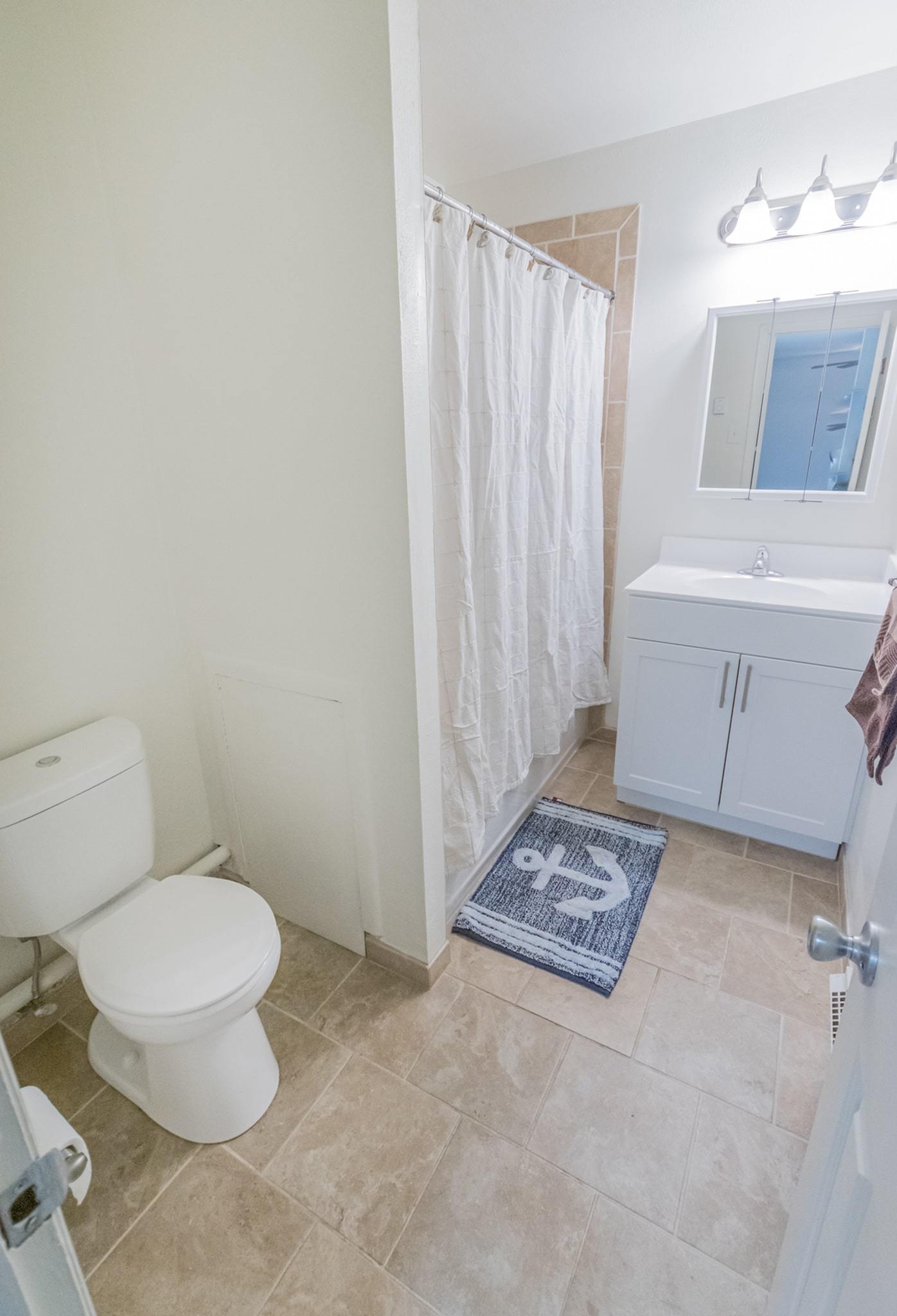 Bathroom with a toilet, sink, mirror, and beige tile flooring.