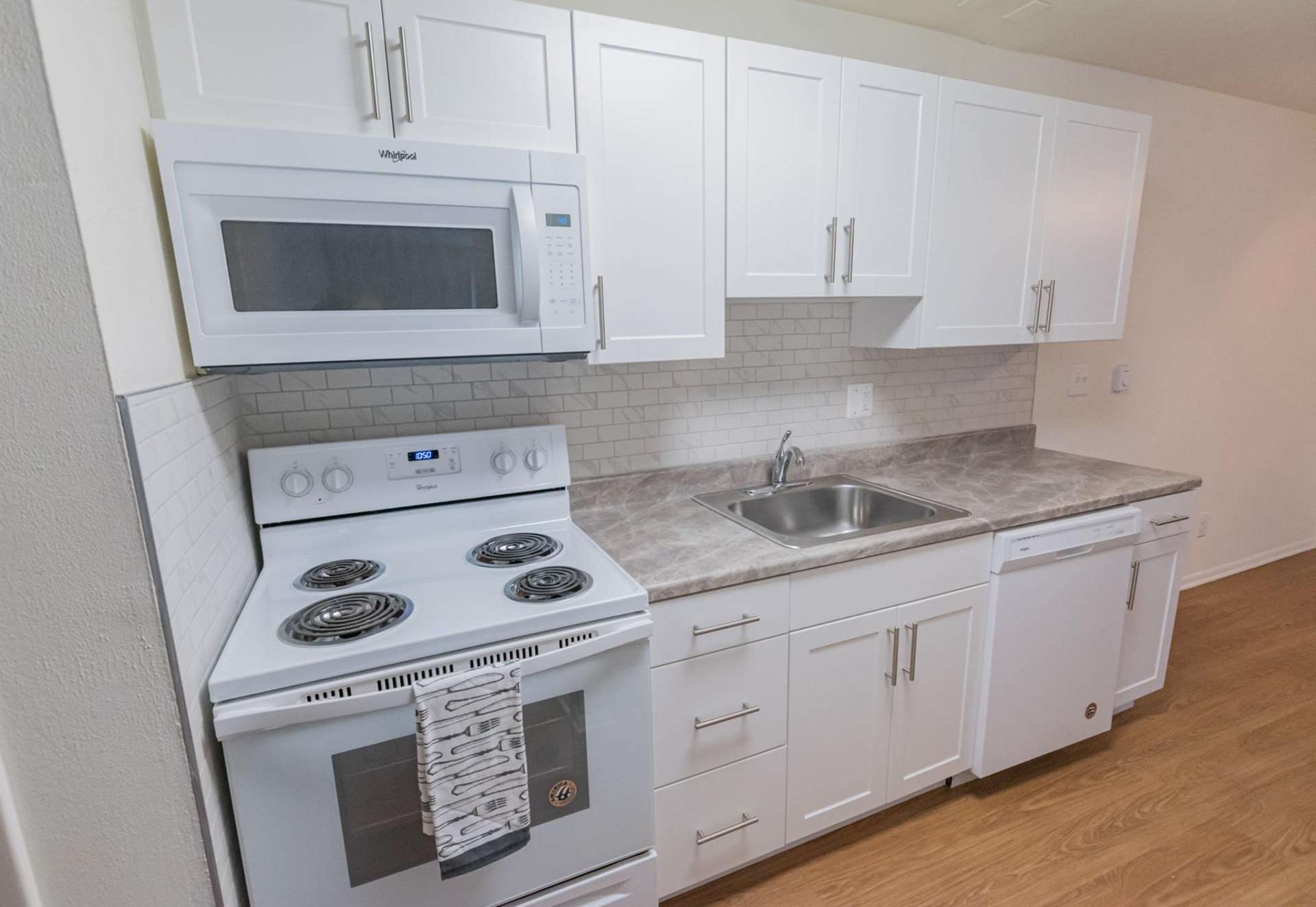 Kitchen area with a dishwasher, stovetop oven, microwave, and white cabinets in an apartment at Hollow Run.