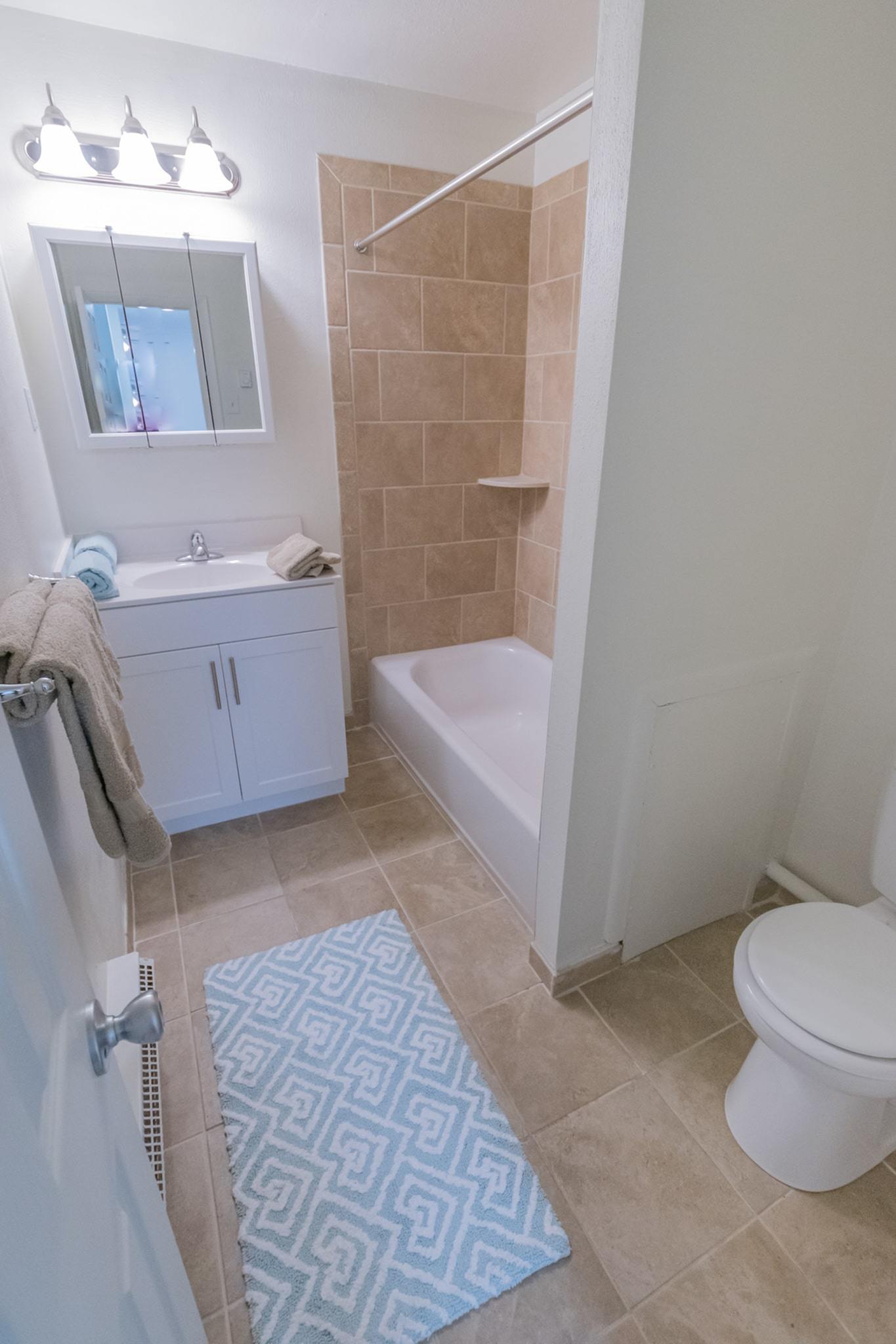 Bathroom with a mirror, bathtub, toilet, and beige tiles.