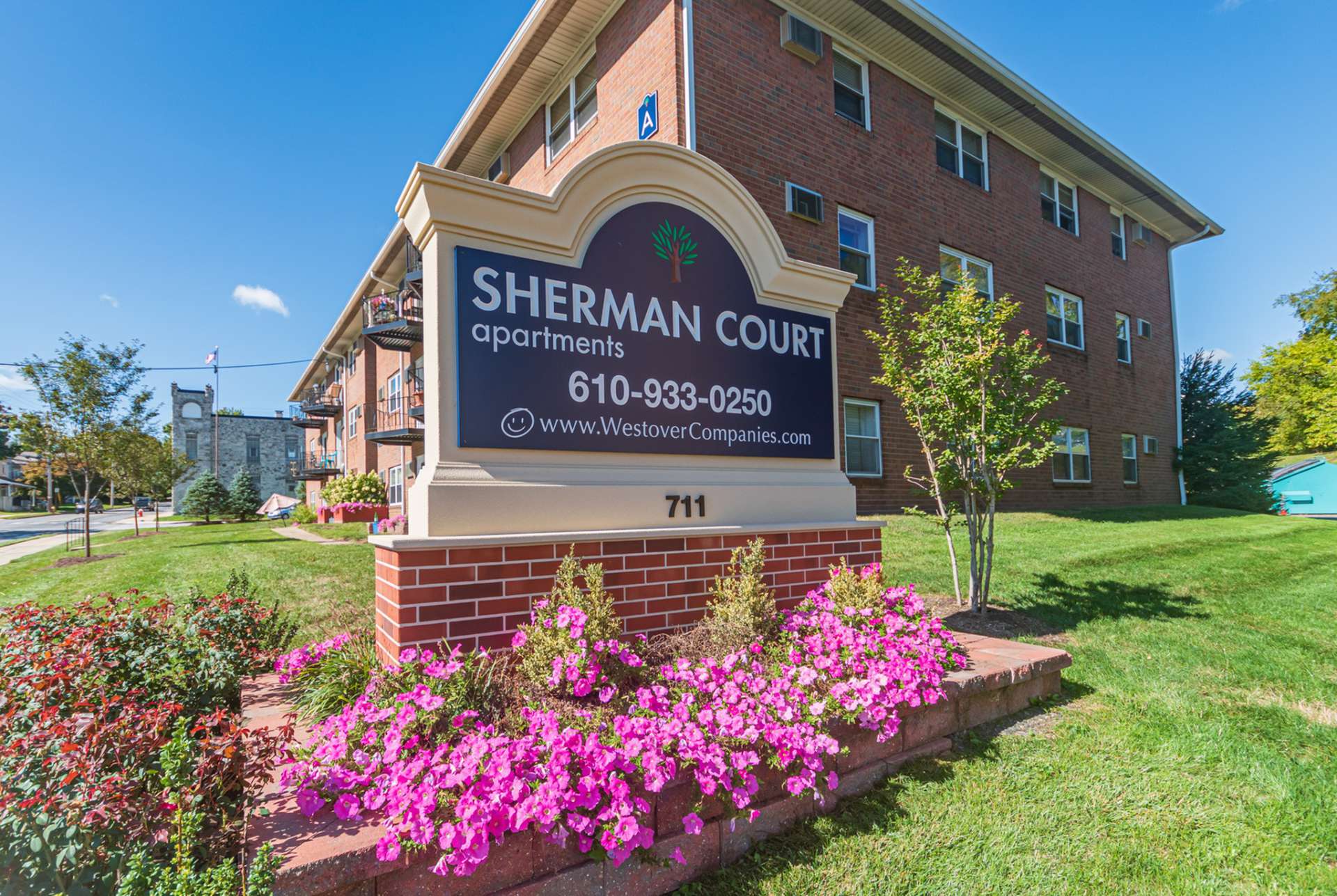 Sherman Court Apartments sign with various flowers around the sign during the daytime.