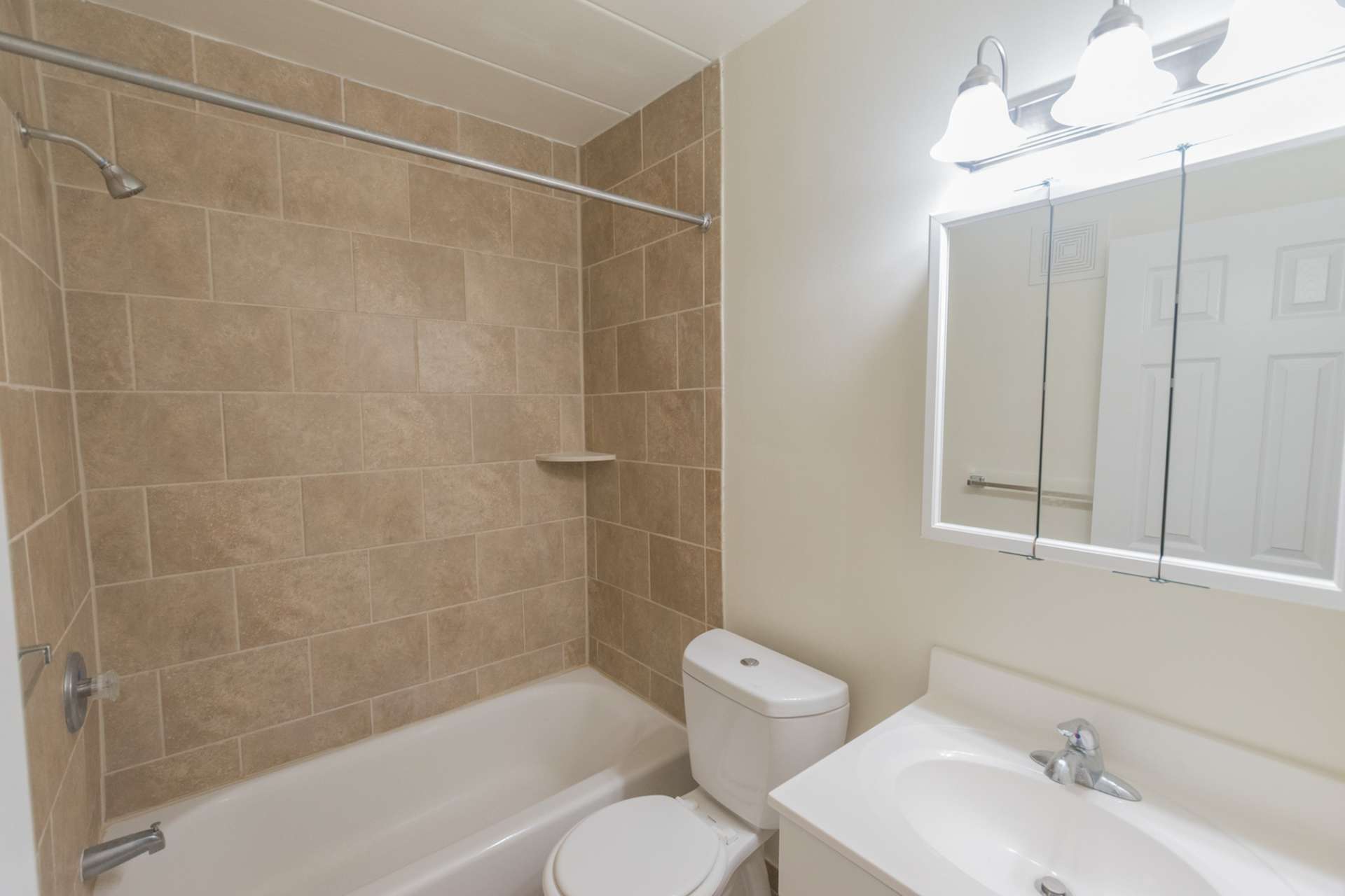 Bathroom with light brown tiles, a bathtub, a mirror, a sink, and vanity lights.