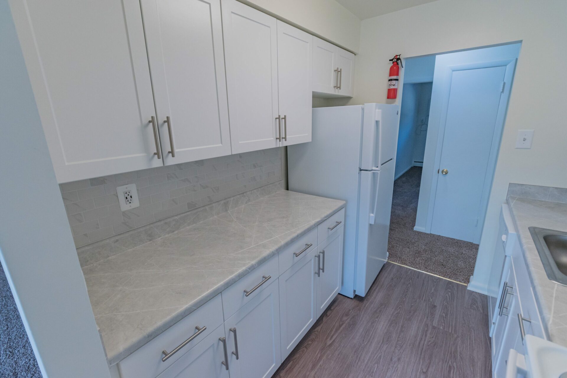 Kitchen area of an apartment, fitted vinyl flooring, a marble counter, a fridge, and a fire extinguisher