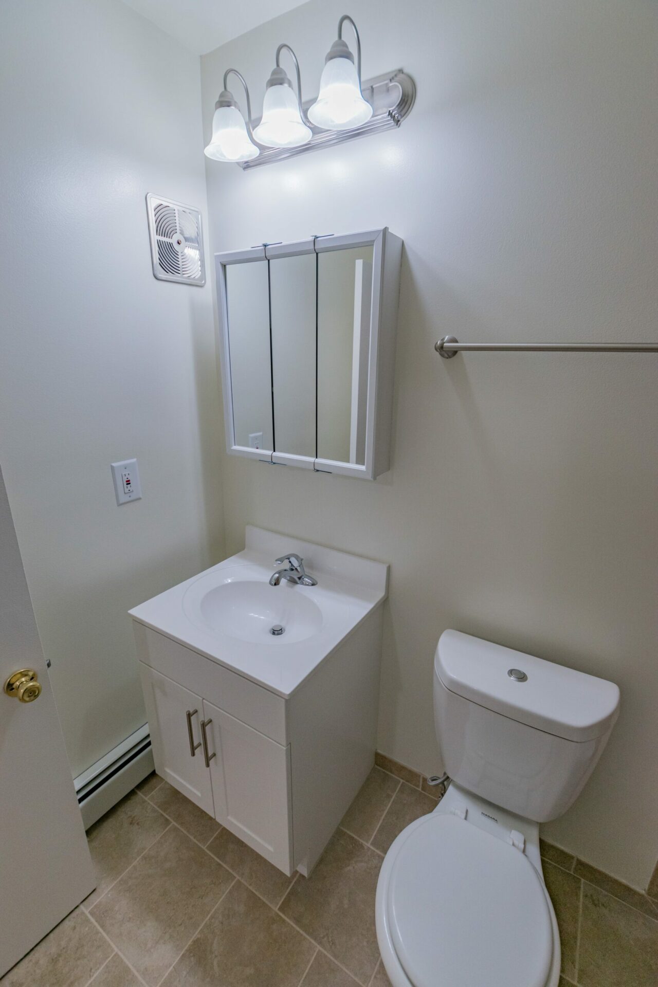 Bathroom area of an apartment, fitted with tiled flooring, single vanity, huge mirror, and a a toilet