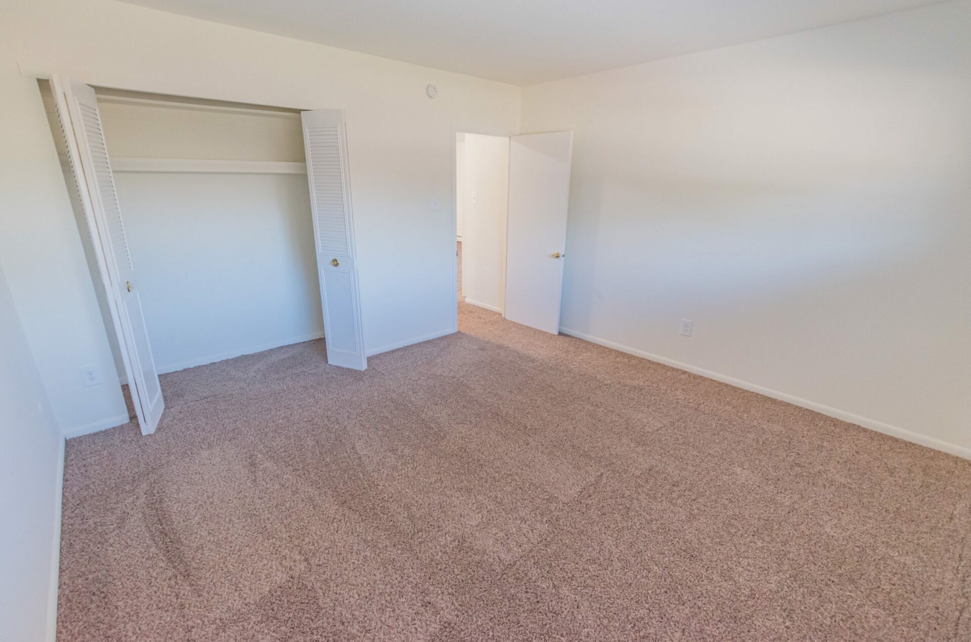 Living room area of an apartment unfurnished, fitted with carpet flooring, a closet, and a doorway to a bed room area