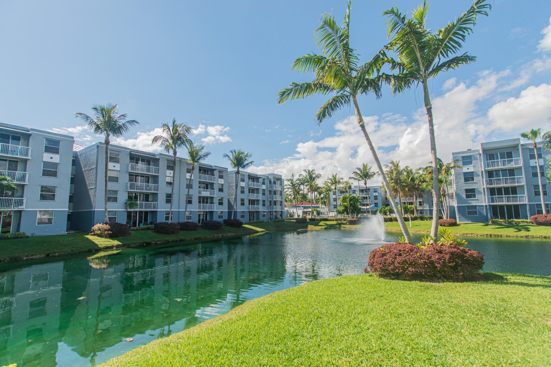 Beachwalk at Sheridan apartment buildings and palm trees surrounding a body of water with a fountain in the middle.