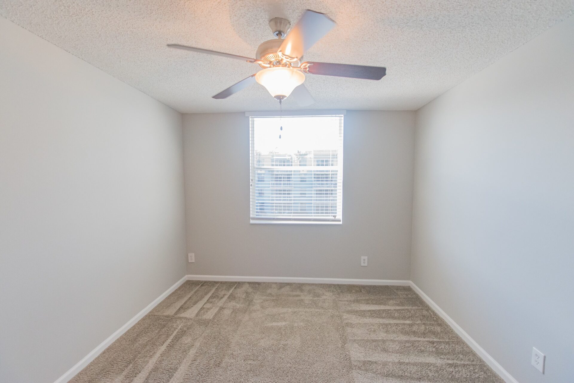 Carpeted room with a window and a ceiling fan.