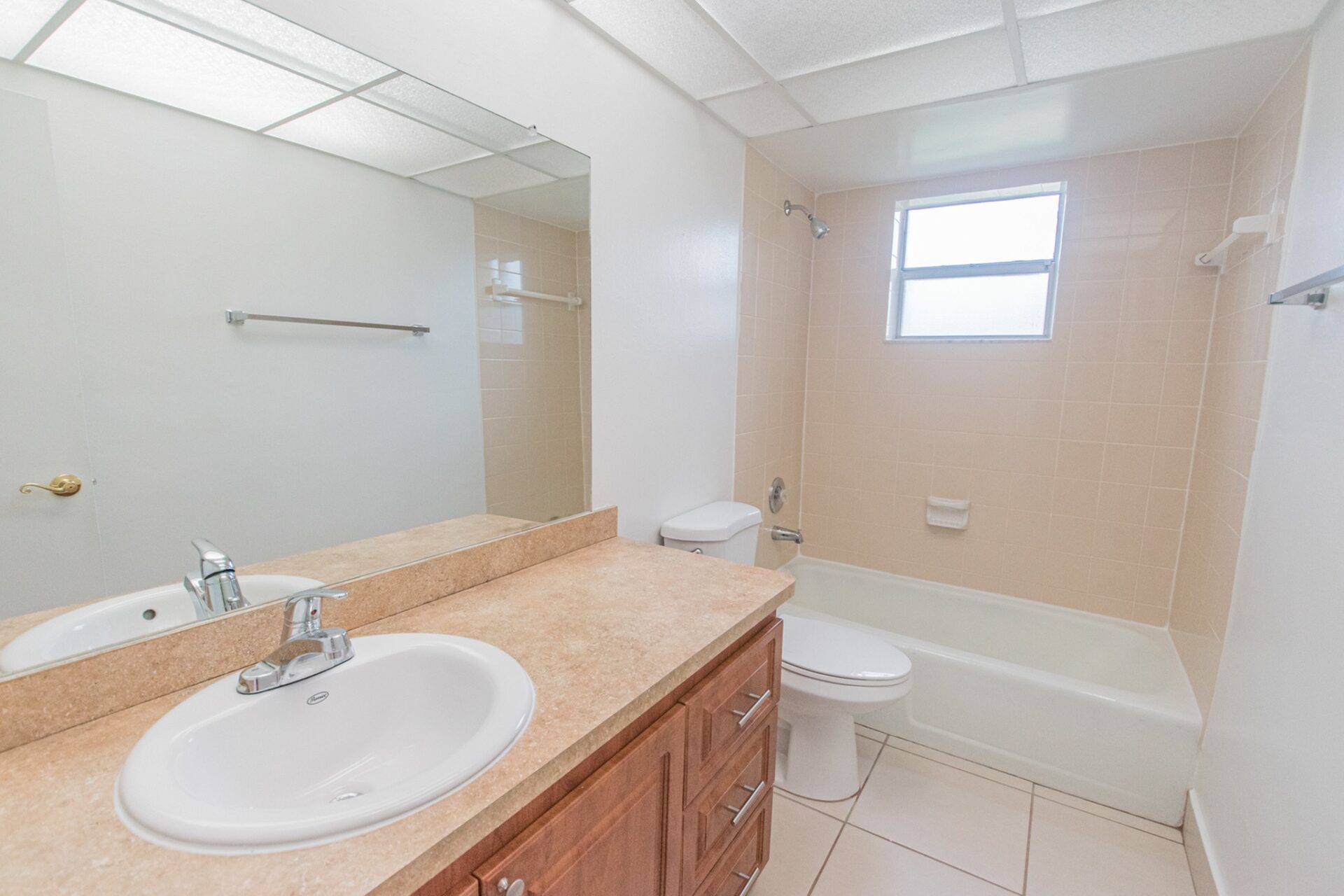 Large mirror with a sink, wooden cabinets, a toilet, and a bathtub in a bathroom.