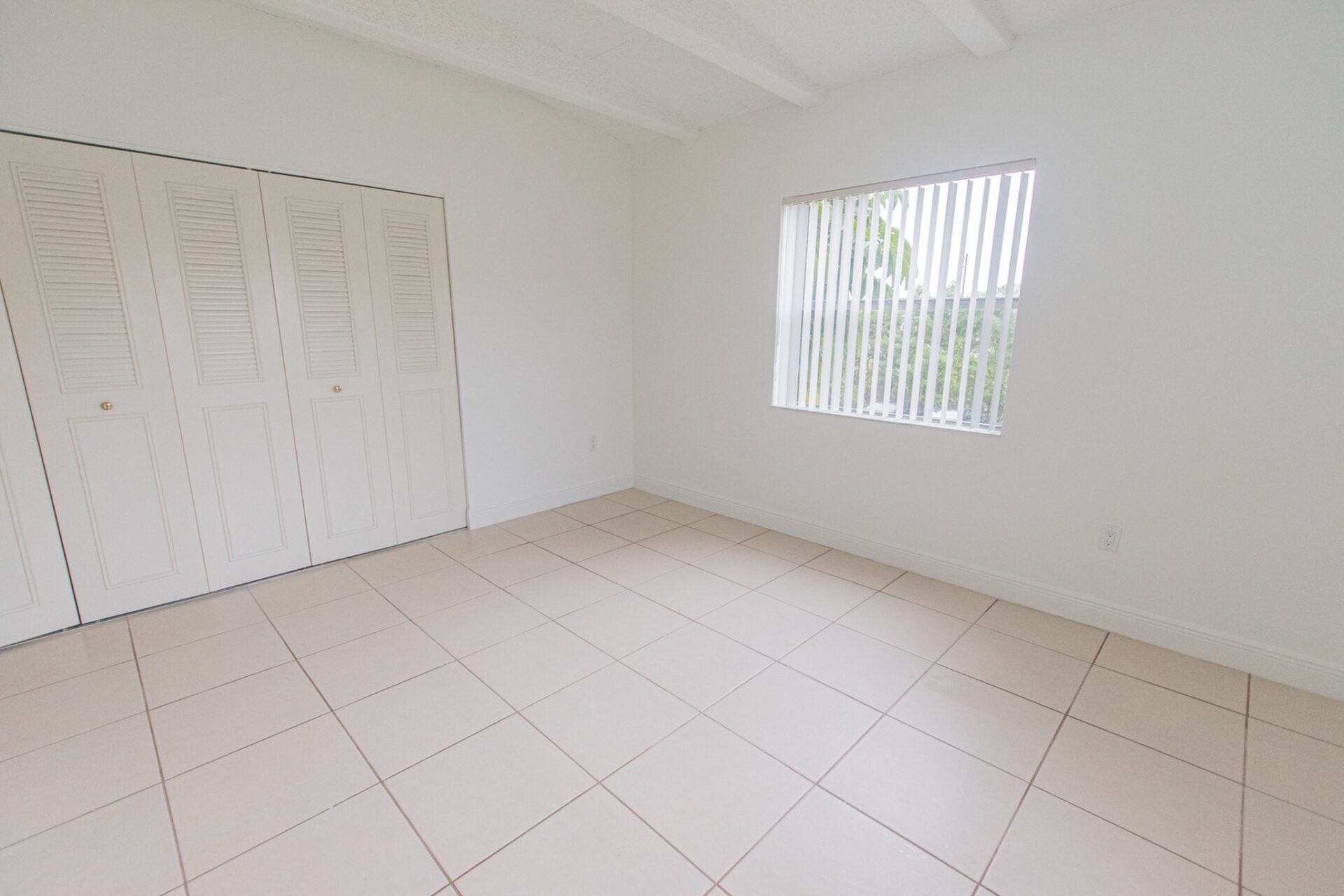 Spacious area in an apartment with a window and white tile flooring.