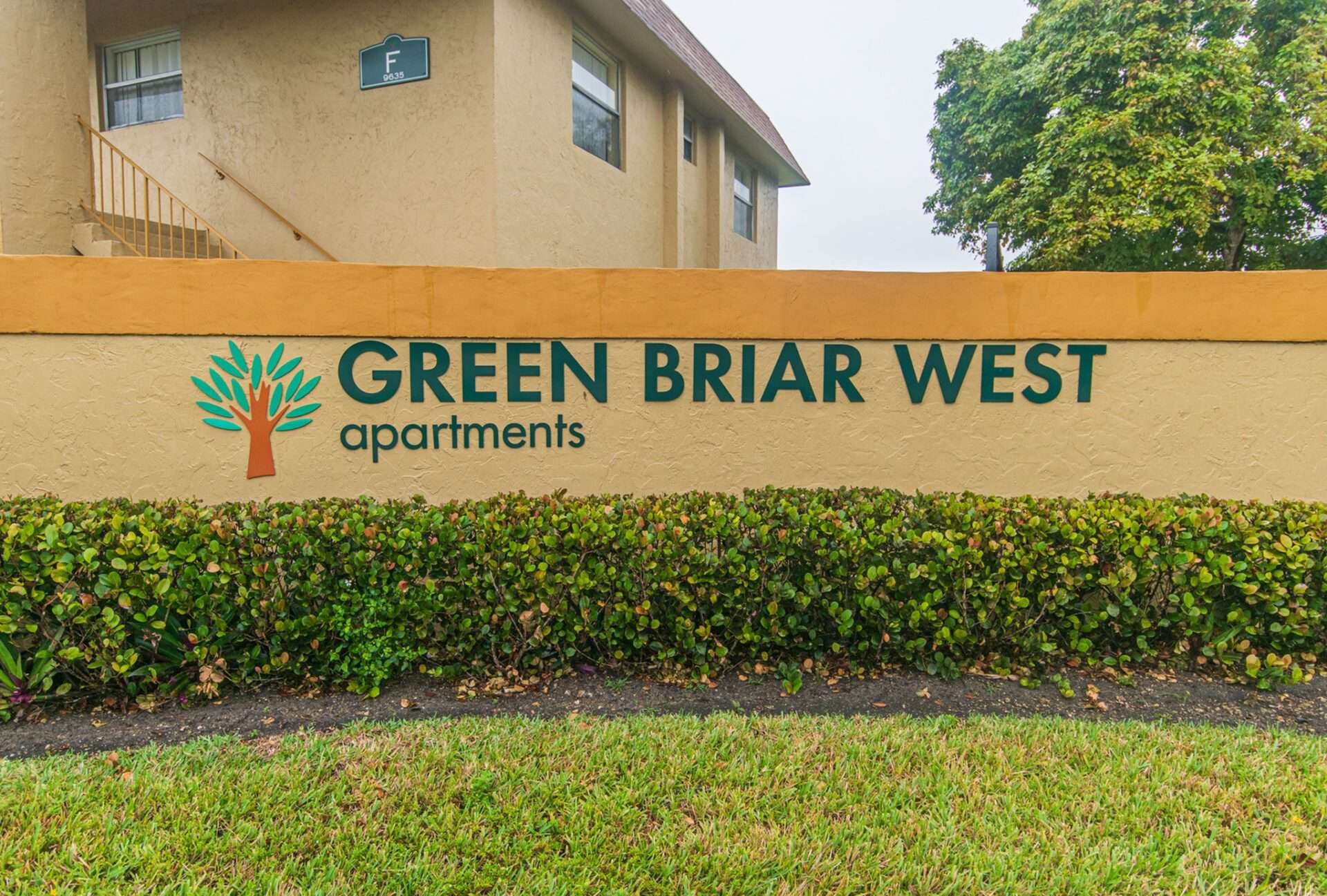 Sign saying "Green Briar West apartments" with landscaped bushes and grass in front of the sign.