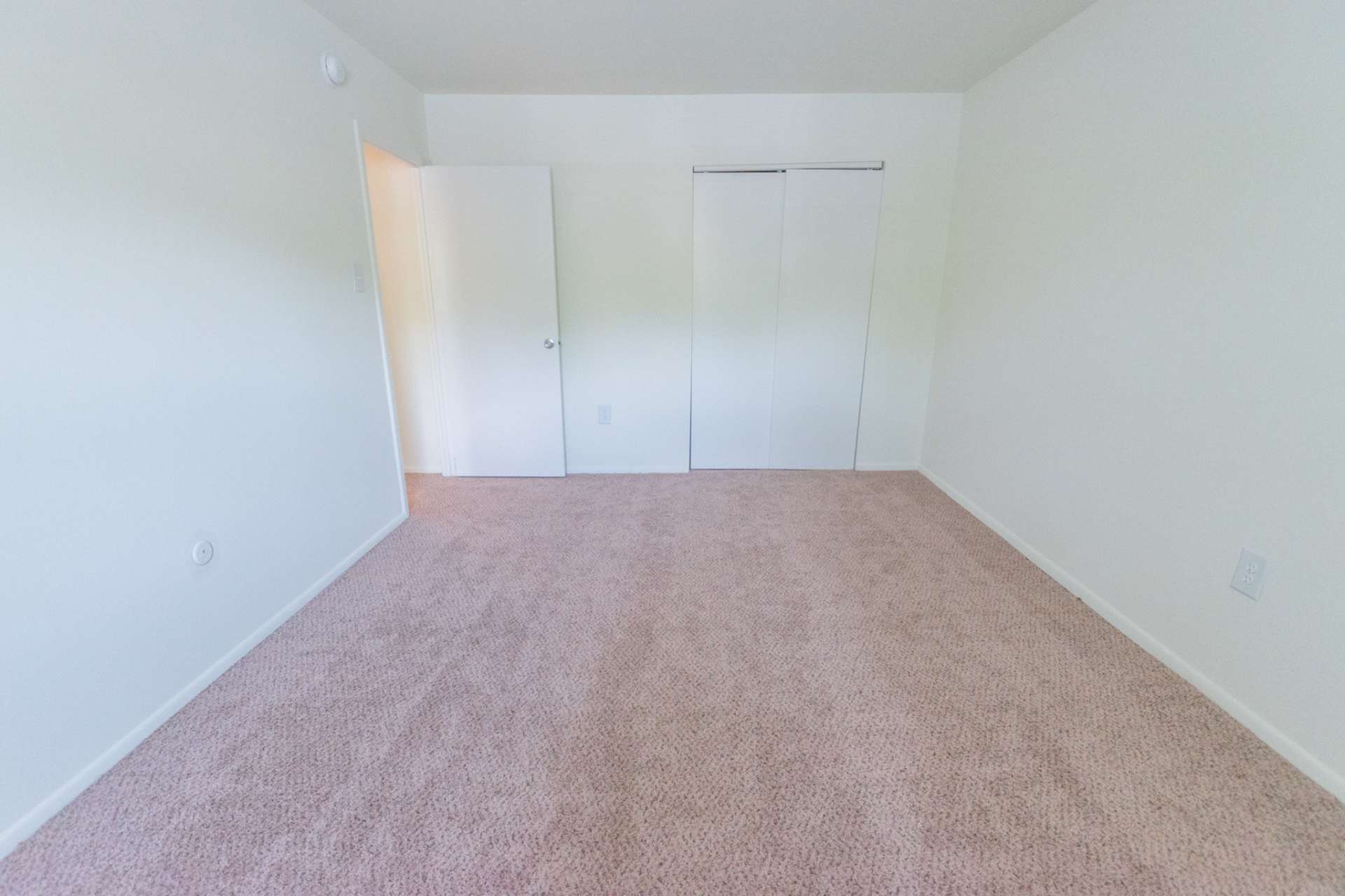 Bedroom with sliding door closet, white walls, and light pink carpet.