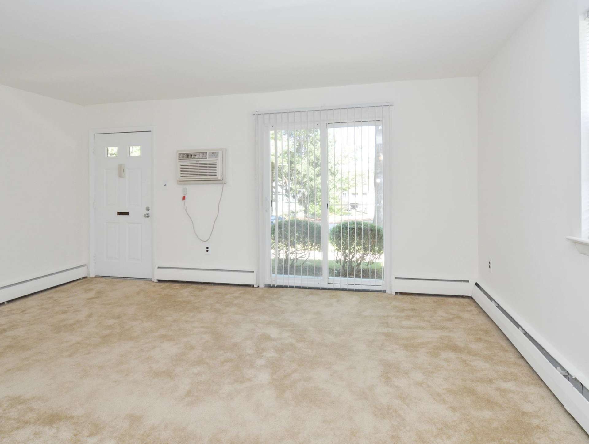 Spacious living room area with beige carpets and sliding glass doors.