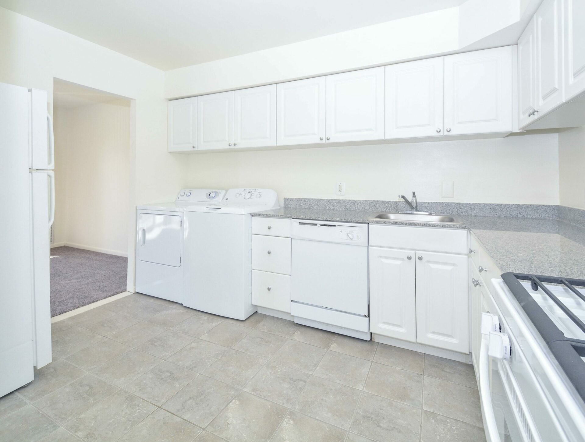 Kitchen area with washer and dryer, white appliances, and white cabinets.