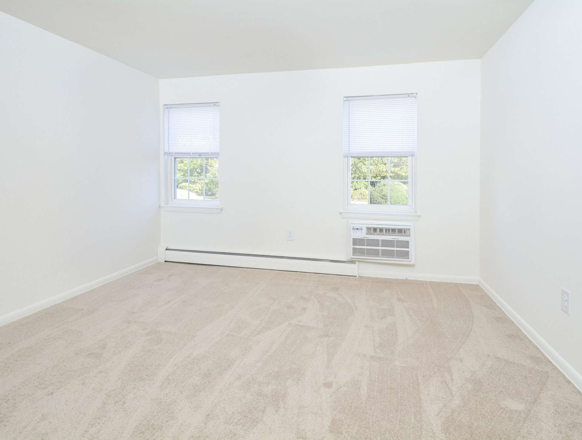 Bedroom with beige carpets, 2 windows, and white walls in an apartment at Knollwood Apartments.
