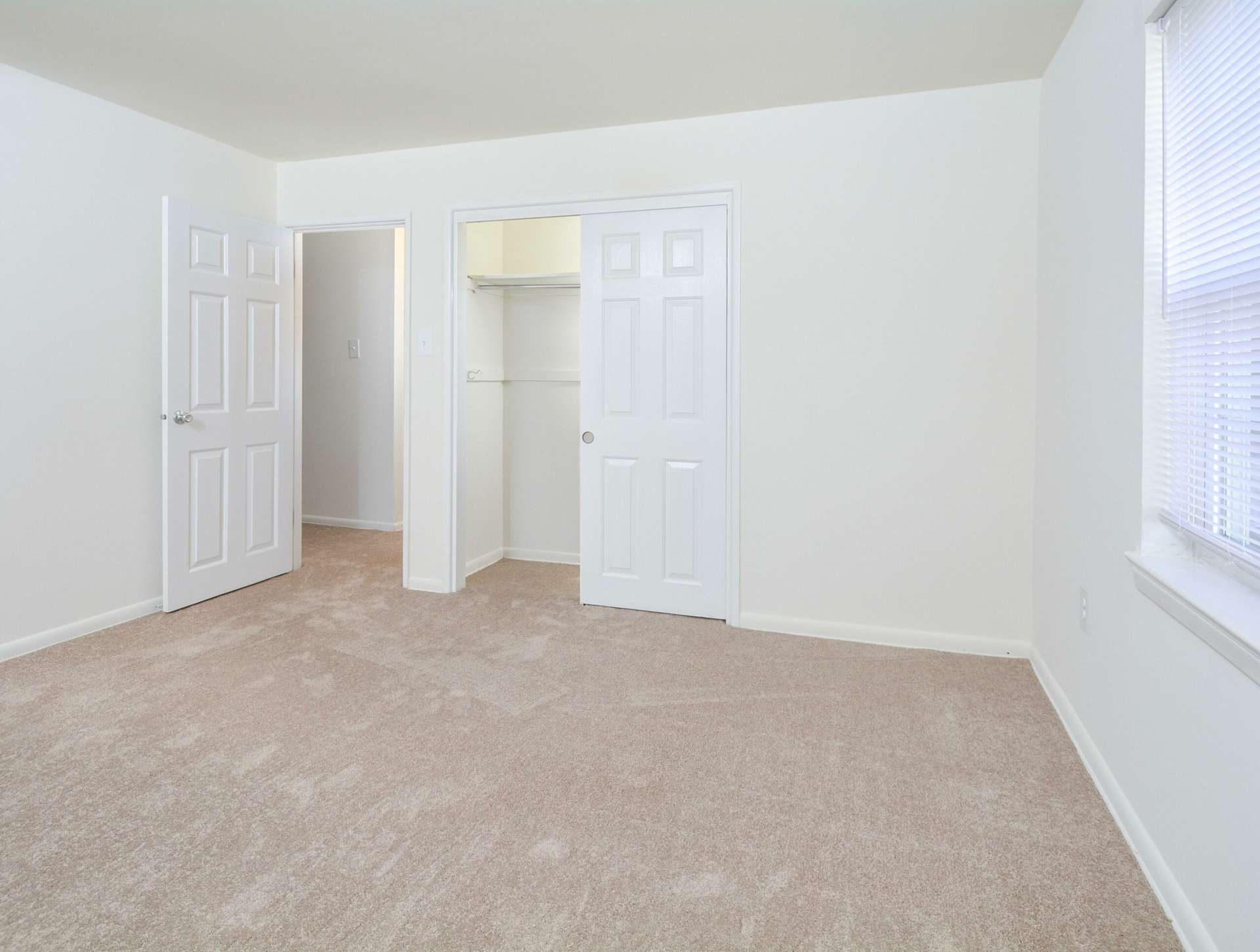 Carpeted bedroom with sliding closet doors and a window.