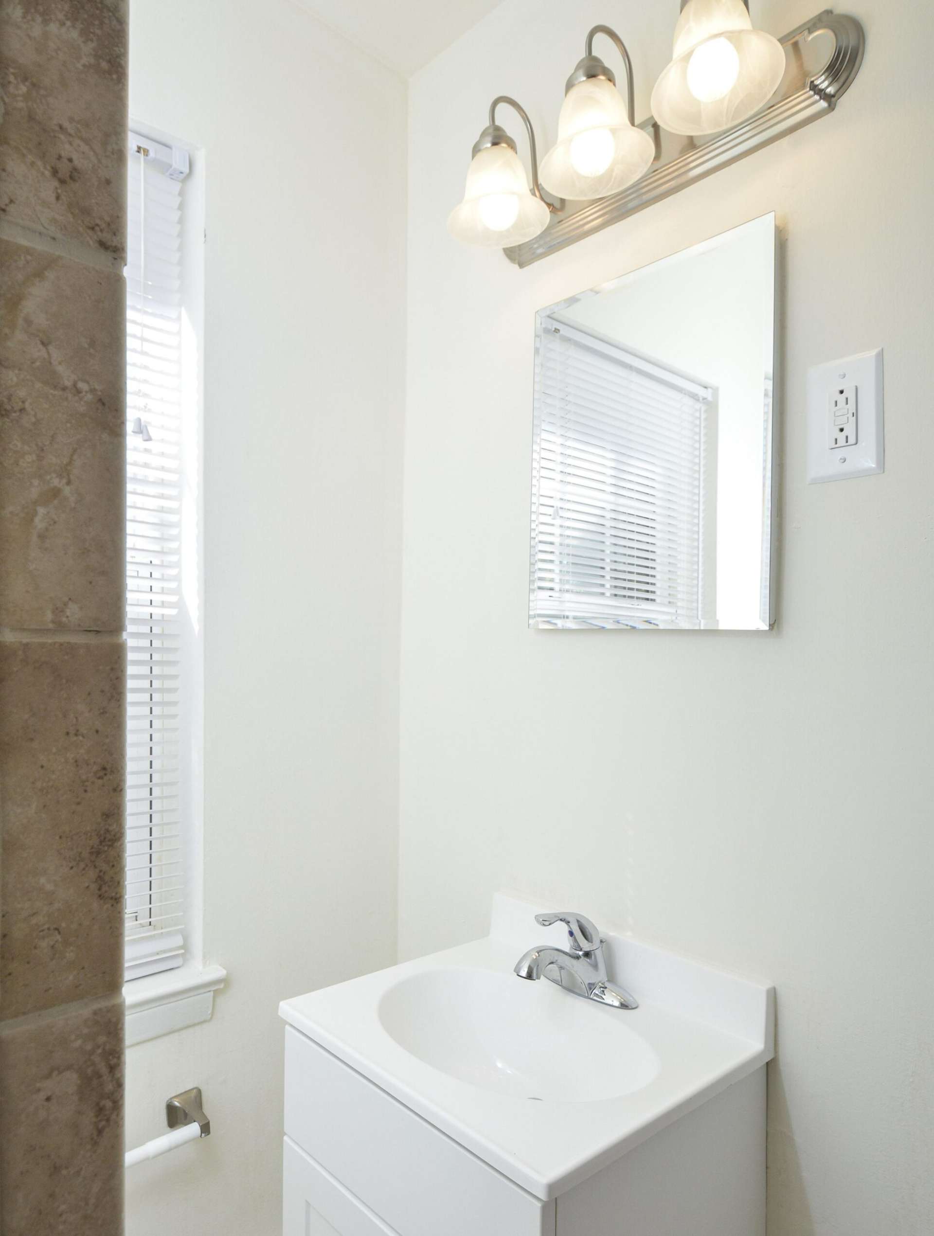Bathroom with a window, small mirror, and sink.