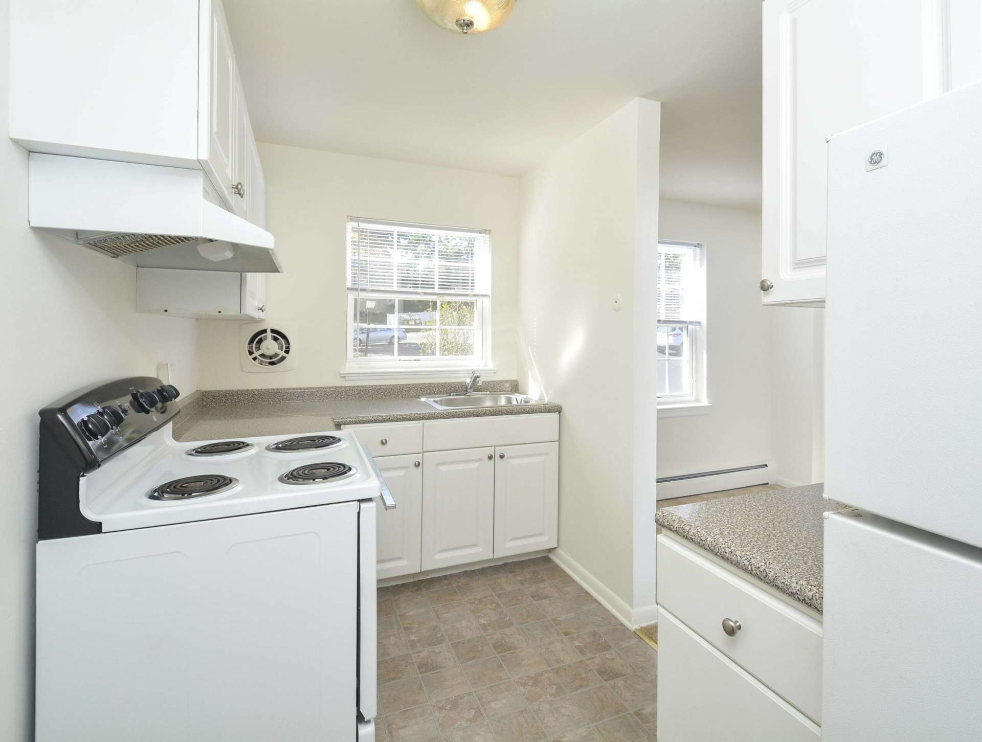 Kitchen with white appliances and white cabinets next to the living room area.