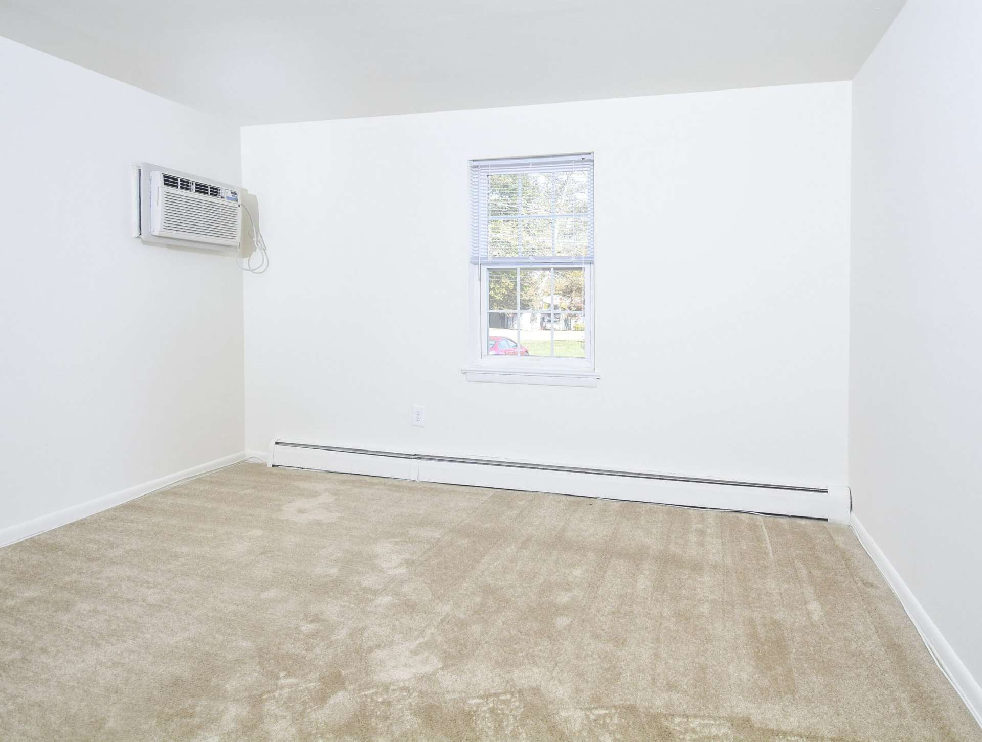 Bedroom with a window, white walls, and beige carpets in an apartment at Knollwood Apartments.