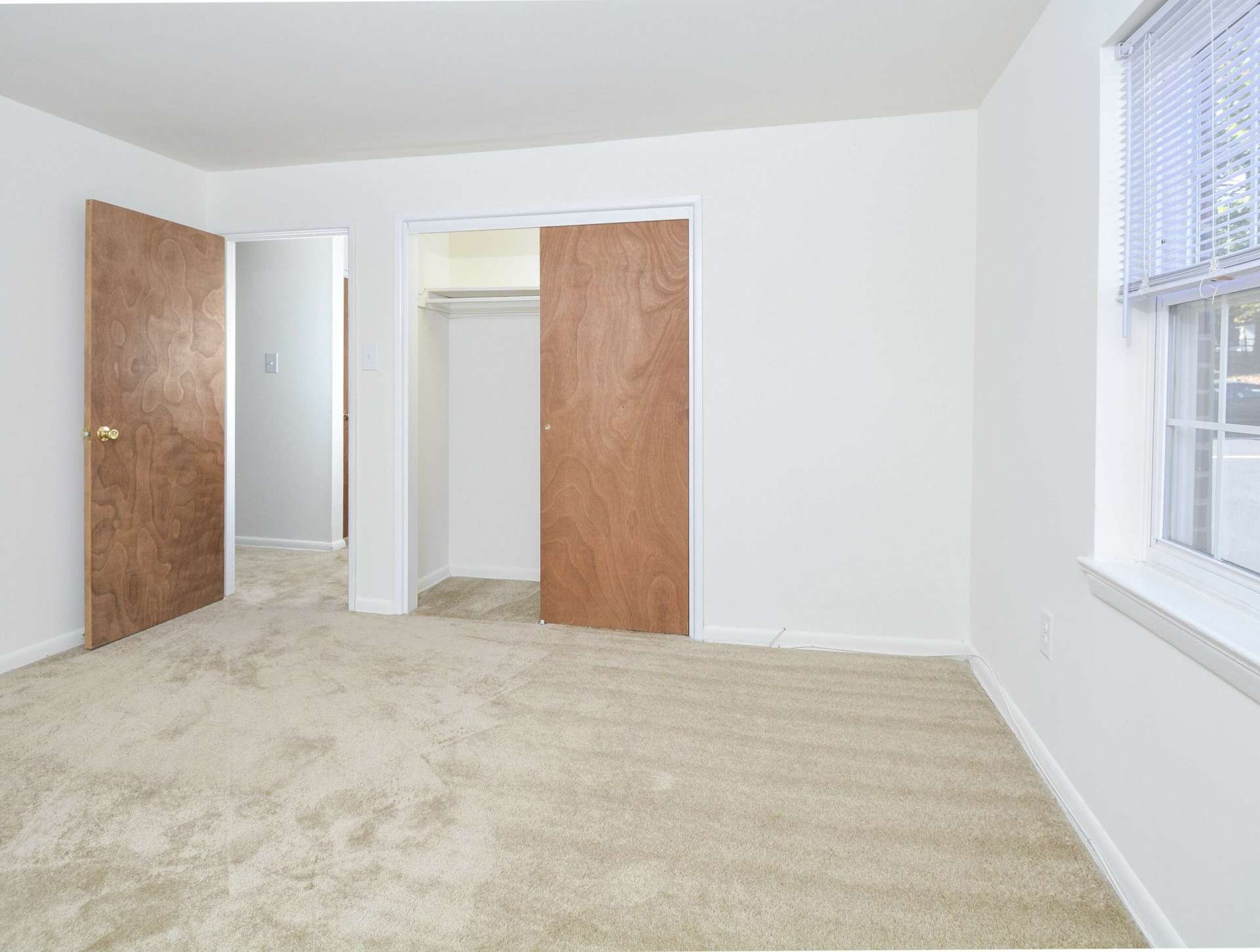 Spacious carpeted bedroom with sliding closet doors and a window.
