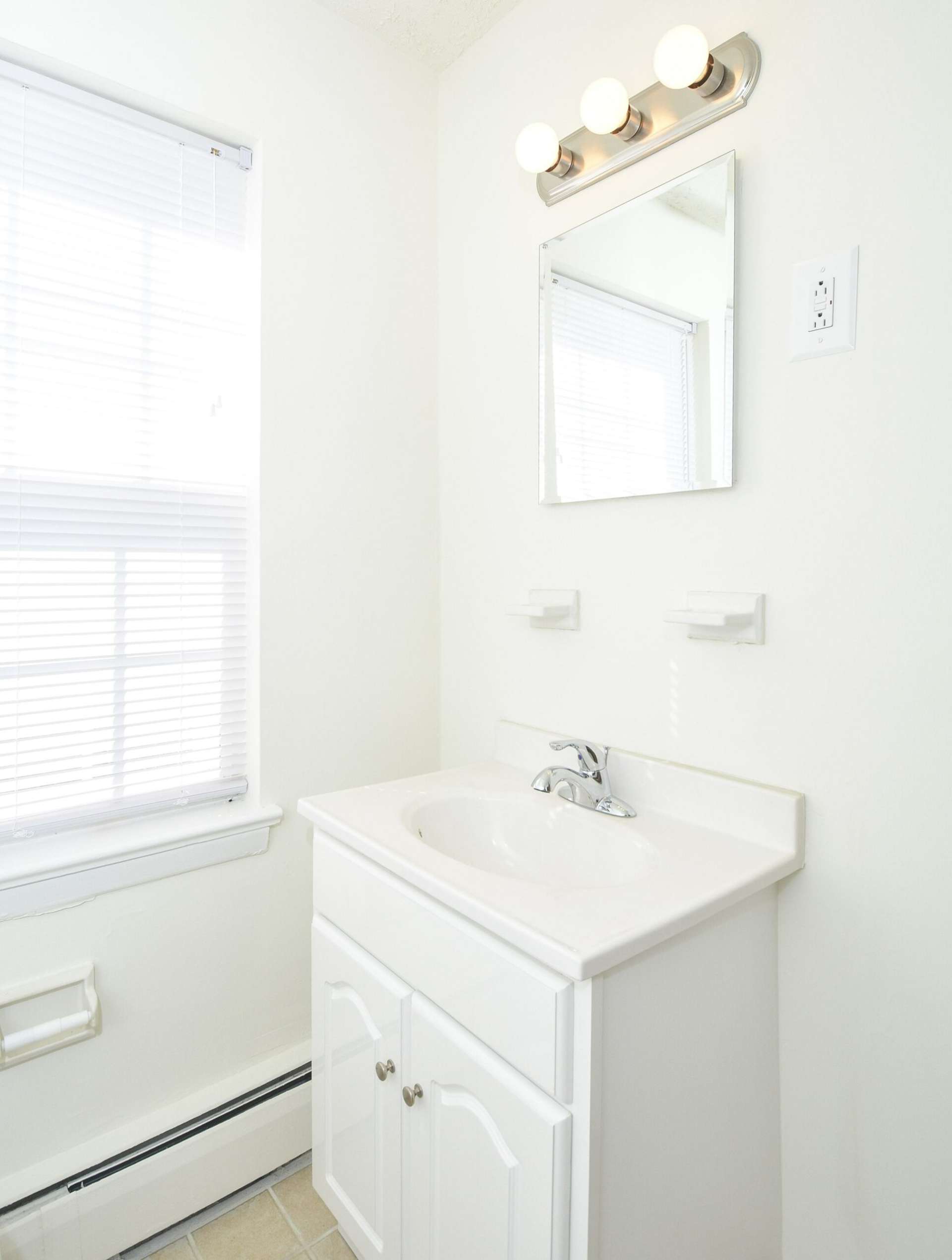 Bathroom with a sink, small mirror, and a large window.