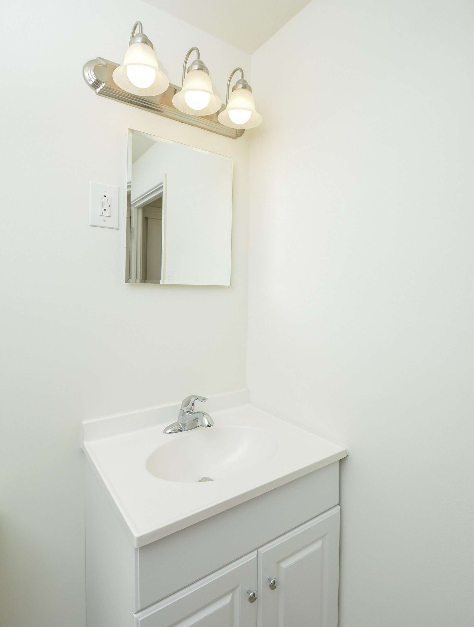 Sink with white cabinets and a small mirror above it.
