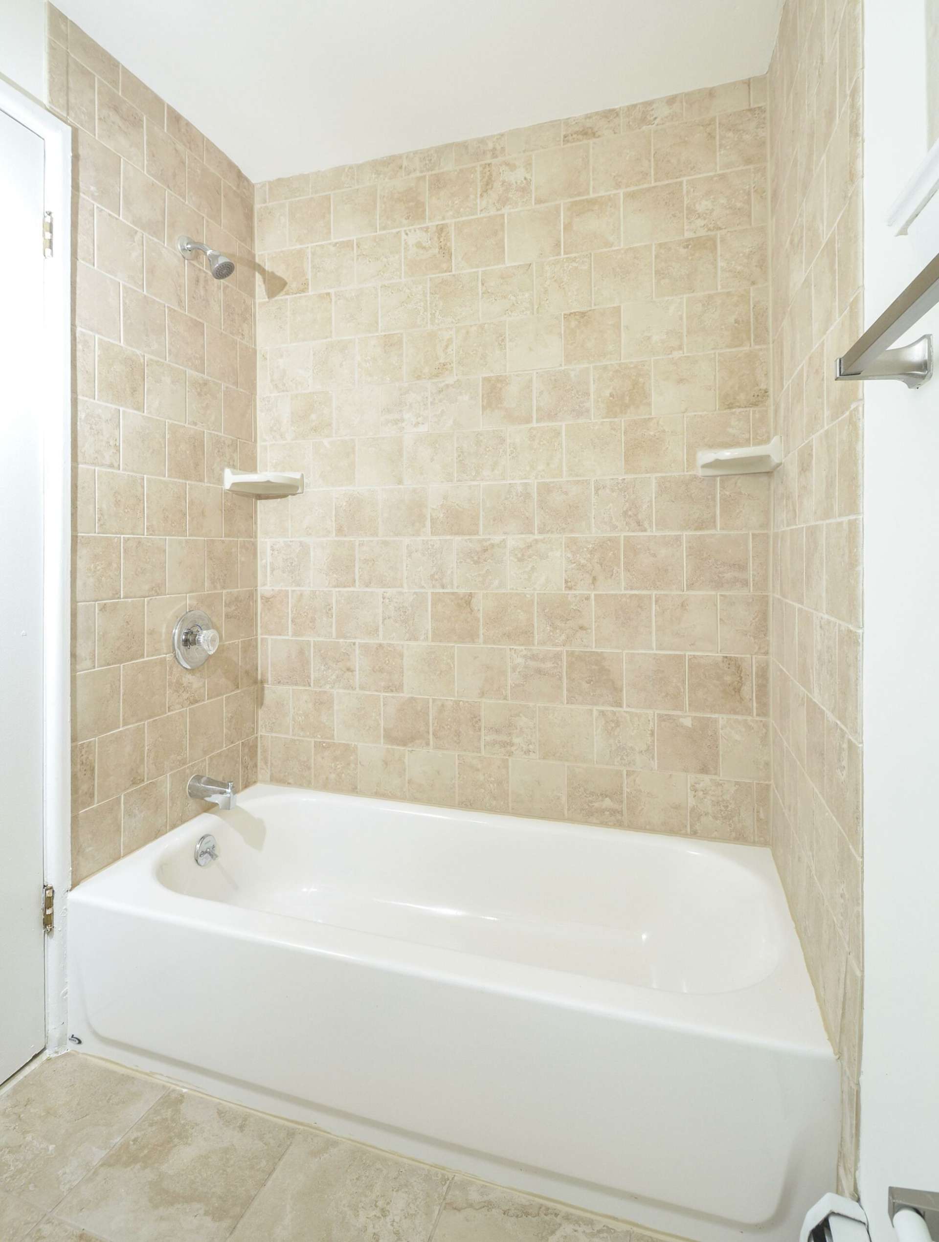 Bathtub with light brown tiles in a bathroom.