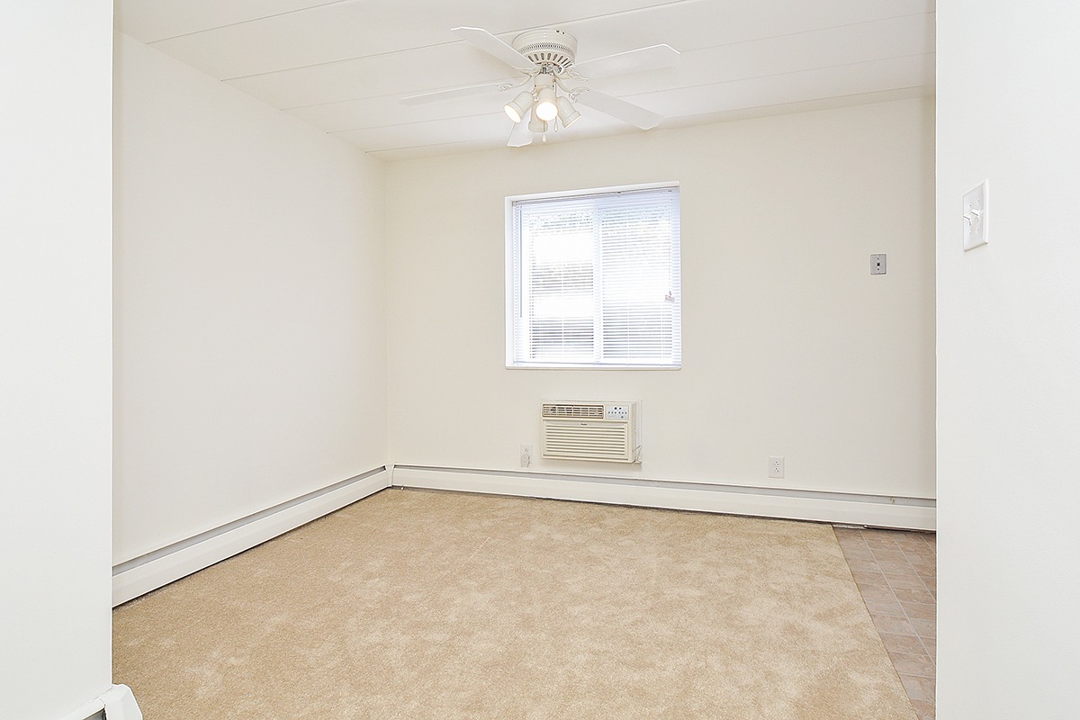 Living area with a window, a ceiling fan, and beige carpets.