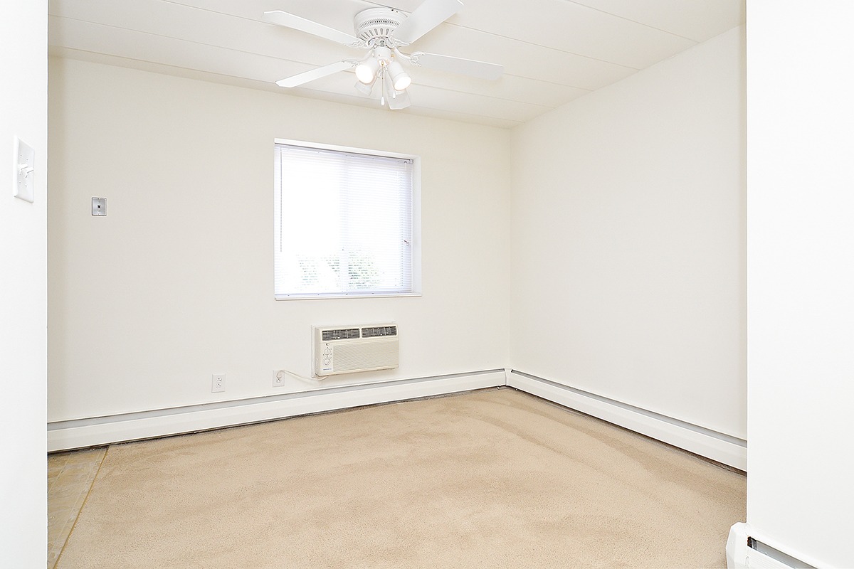 Living area with light beige carpets, a window, and a ceiling fan.