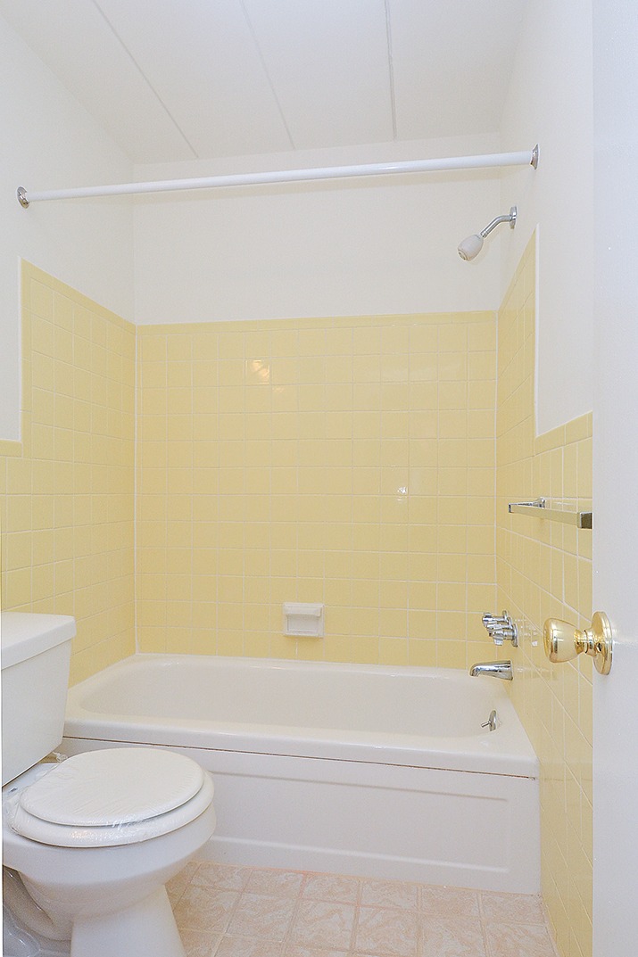 Bathroom with yellow tiles, a bathtub, and a toilet.