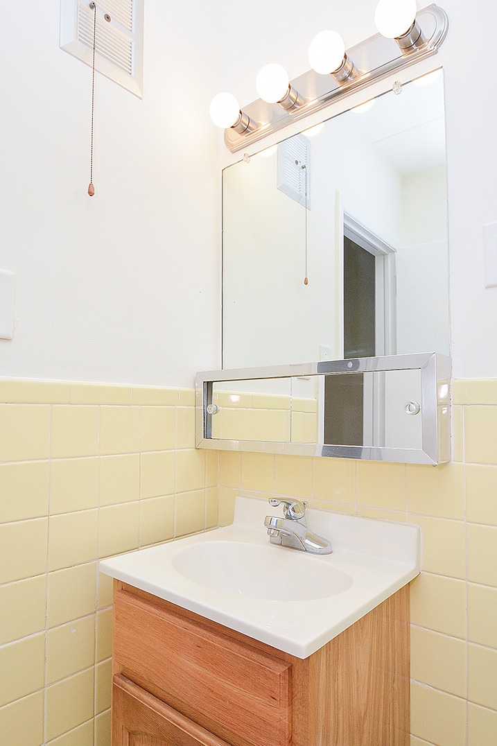 Bathroom with yellow tiles, a mirror, a sink, wooden cabinets, and vanity lights.