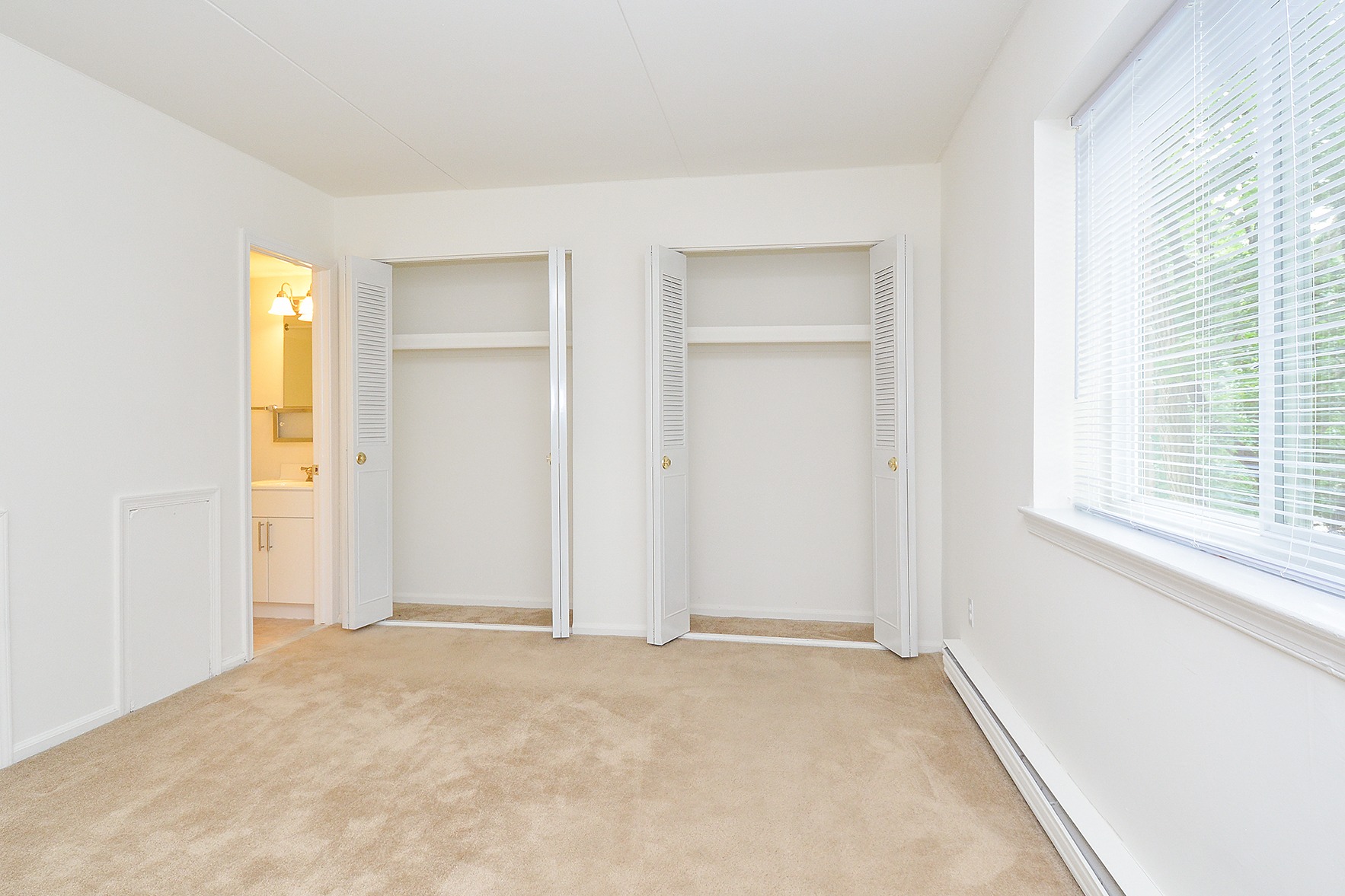 Carpeted bedroom with a large window, closet space, and a bathroom connected.