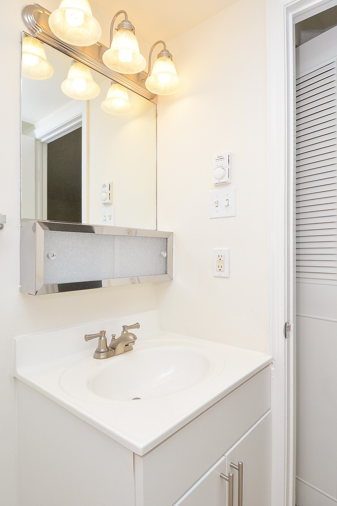 Sink with white cabinets, mirror, and 3 lights above the mirror in a bathroom.