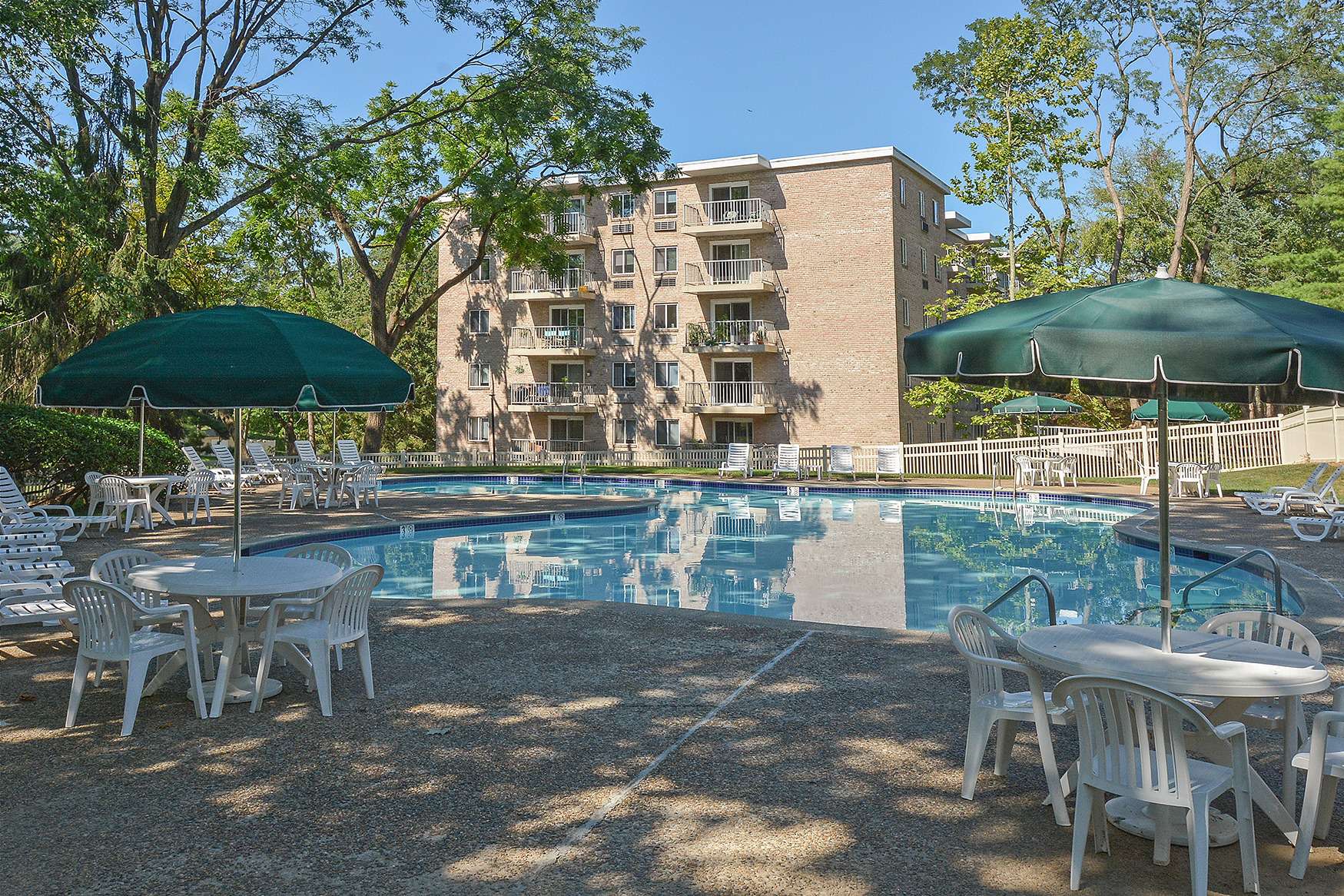 Outdoor pool area with a variety of seating options surrounded by trees and apartment buildings.