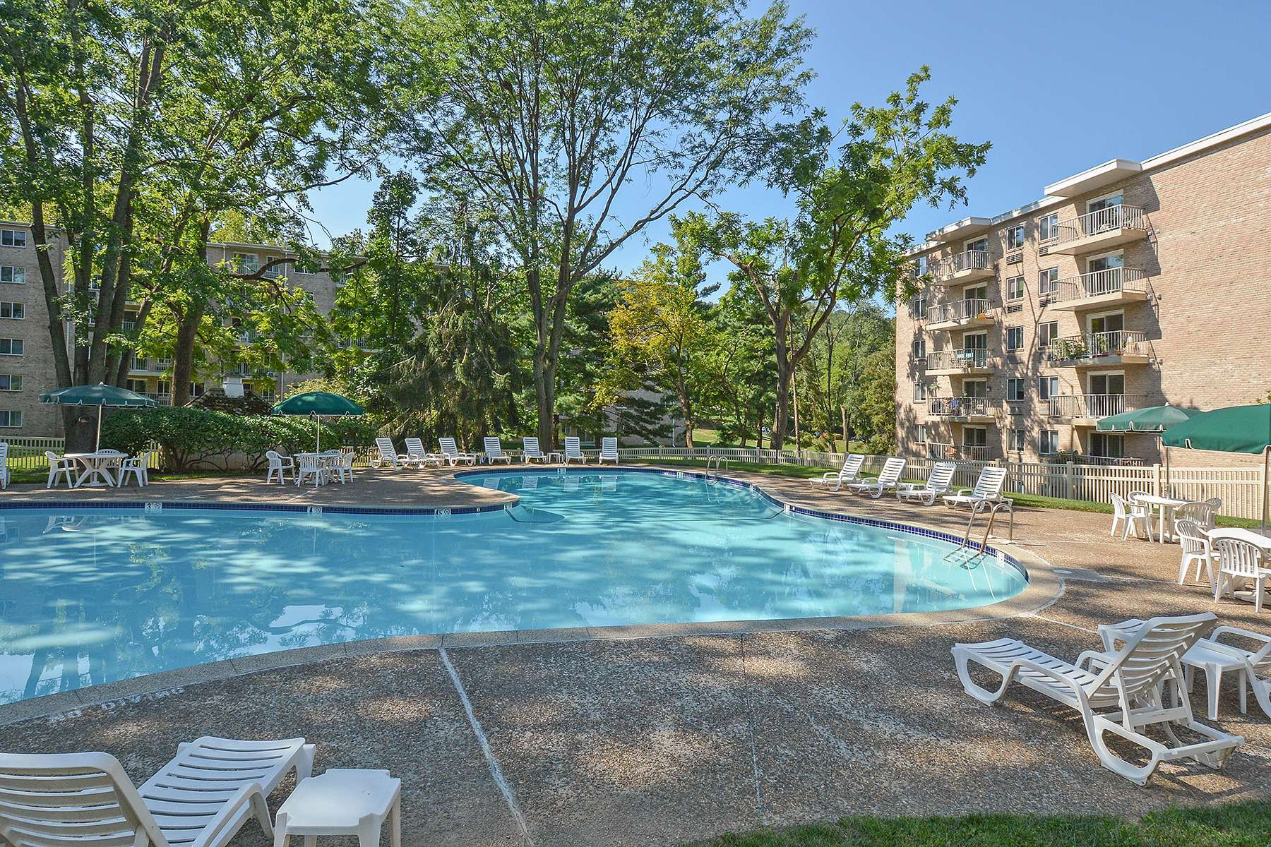 Fenced-in pool area surrounded by trees and apartment buildings.