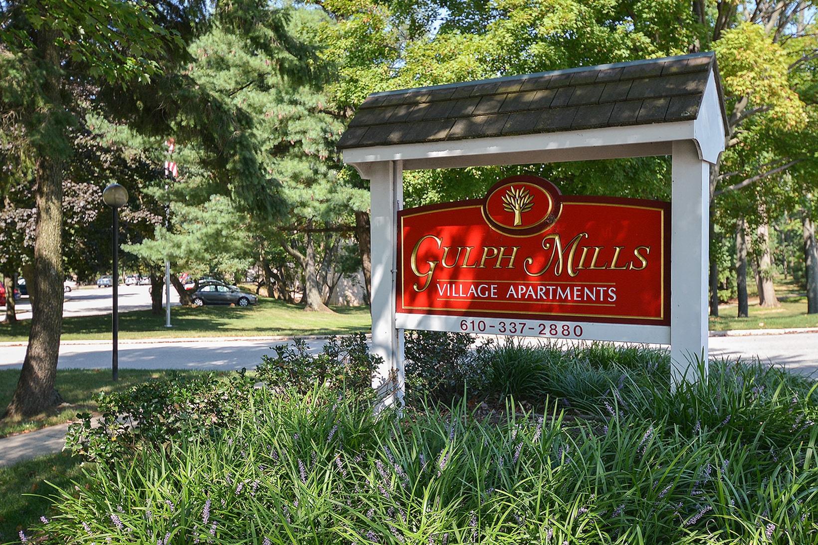 Gulph Mills Village Apartments sign on grass with trees surrounding the sign during the daytime.