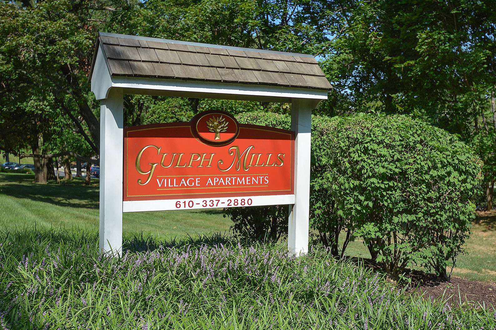 Gulph Mills Village Apartments sign on grass with trees surrounding it.
