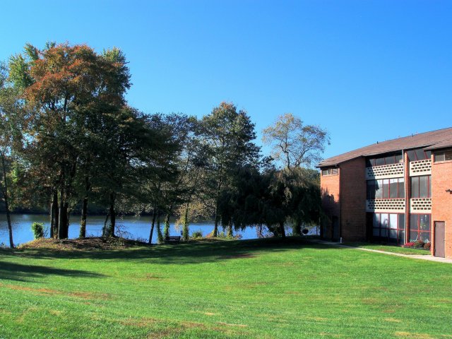 Exterior of an apartment building with a spacious grass area, trees, and a lake.