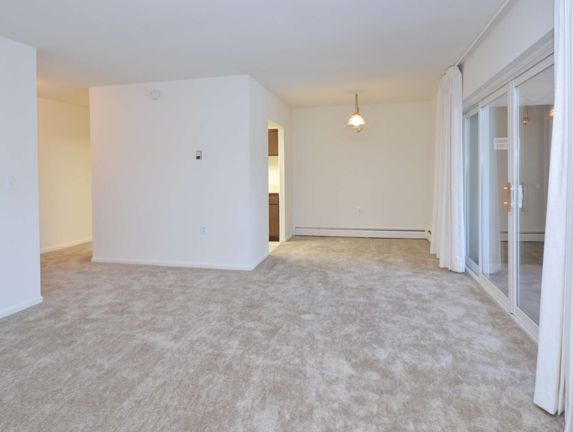 Spacious living room area with white carpets and sliding glass doors to the balcony.