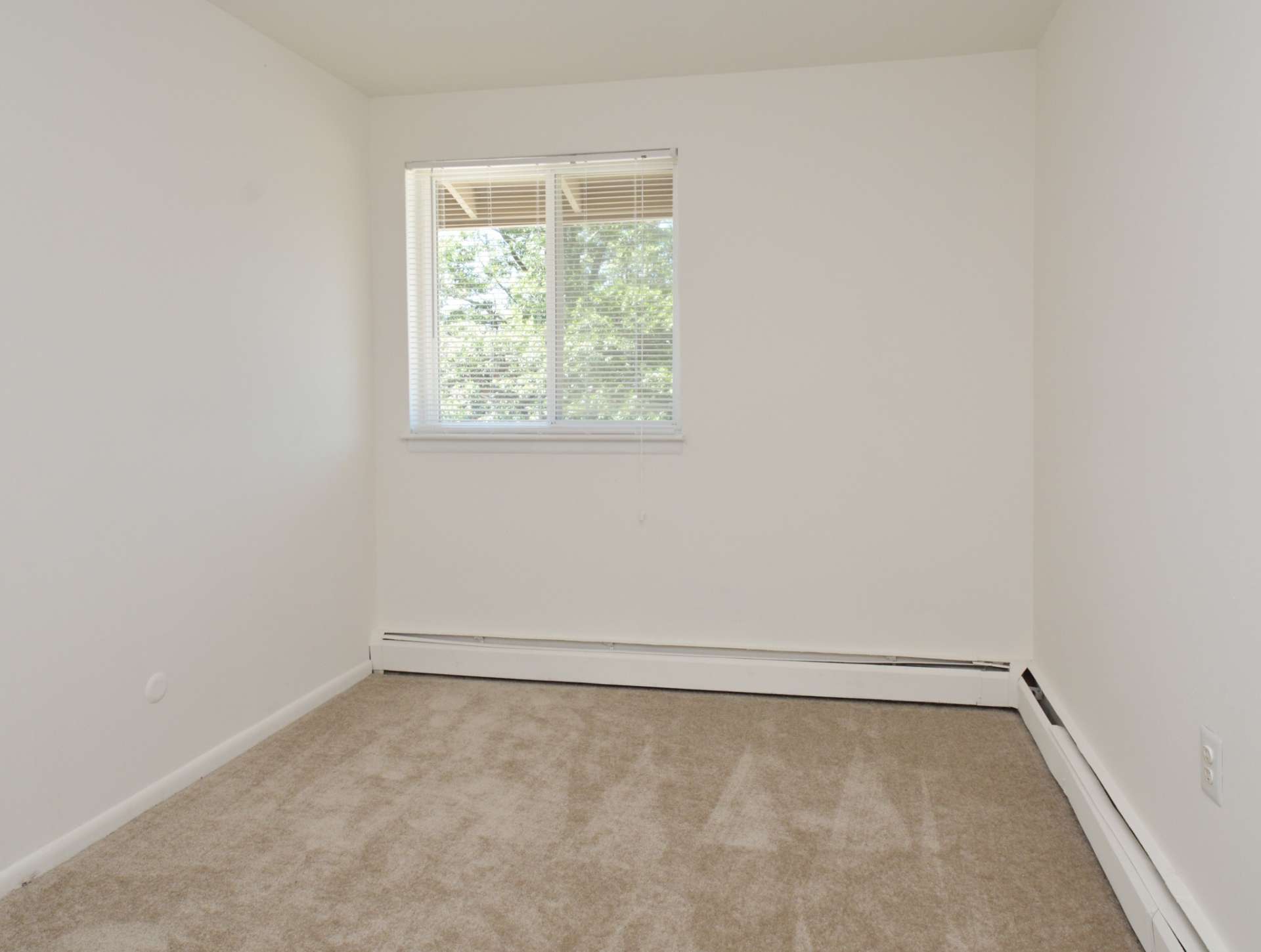 Bedroom with white walls, a window, and beige carpets.