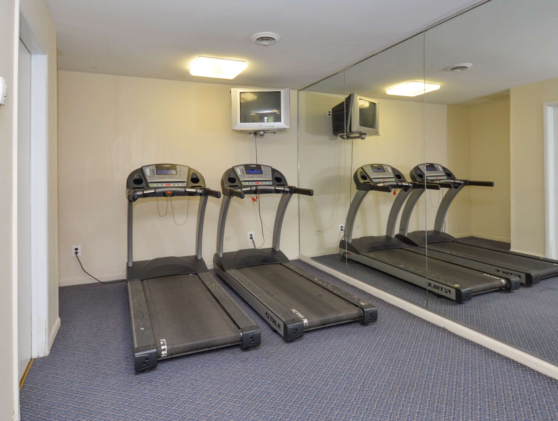 Two treadmills with mirrors on the side wall and a hanging TV at an indoor gym at Glen Eagle Village apartments.