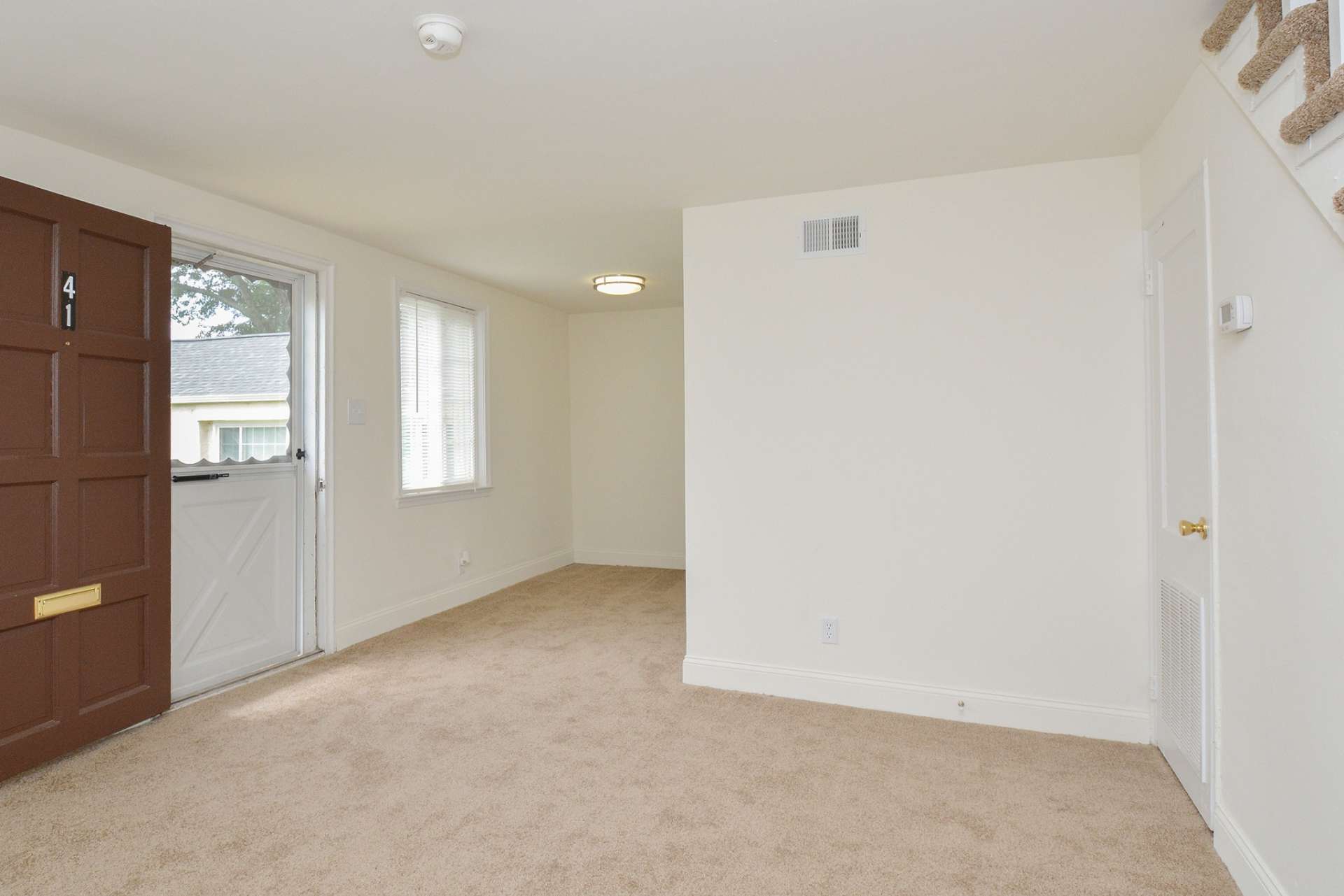 Downstairs of a townhome with large windows and carpeted flooring.