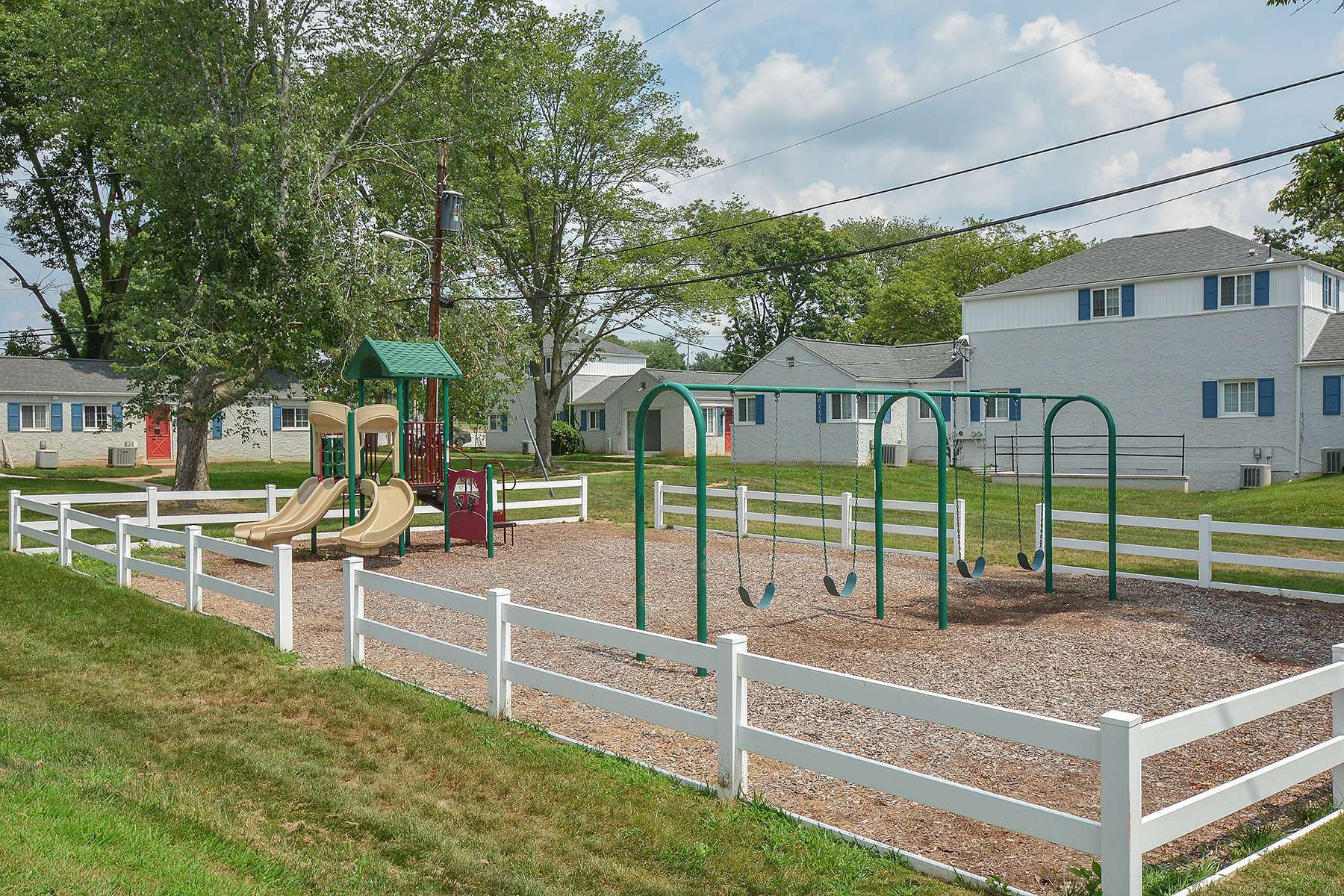 Fenced-in playground on mulch with apartments surrounding the play area.
