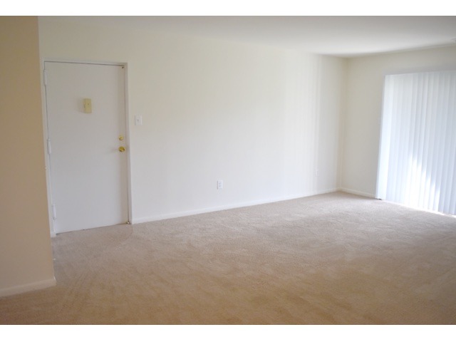 Living room area of an apartment, fitted with carpet flooring, and a sliding door
